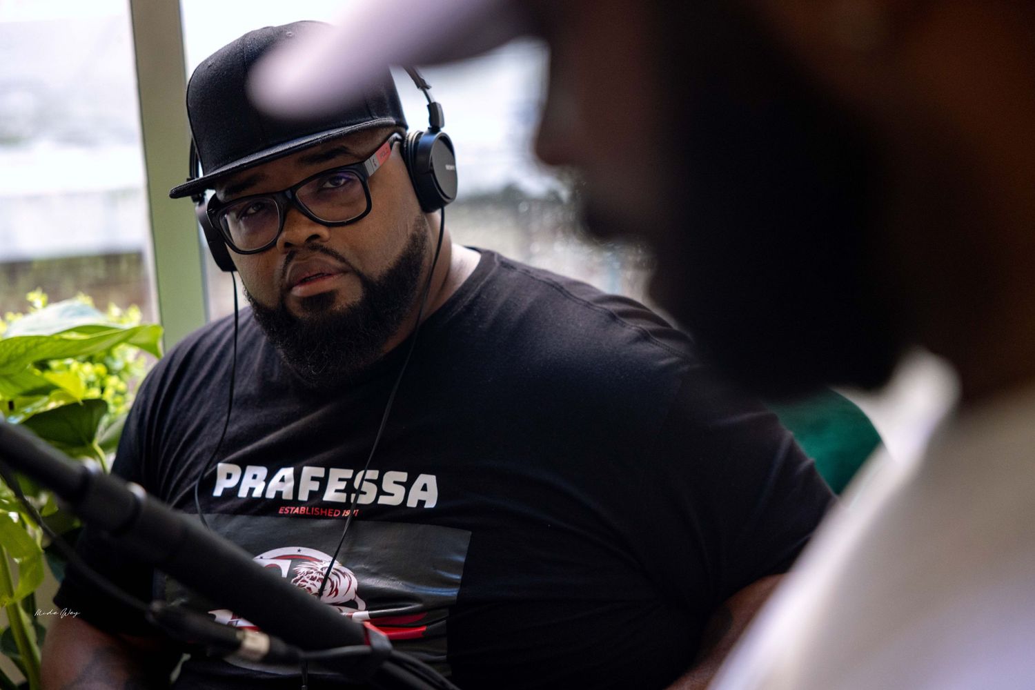 Person wearing headphones and Praffessa t-shirt sitting in recording setup.