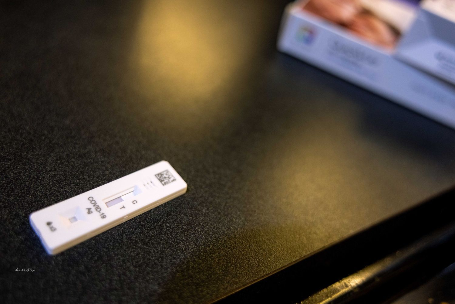 A COVID-19 rapid test device sits on a dark surface with blurred background lighting.