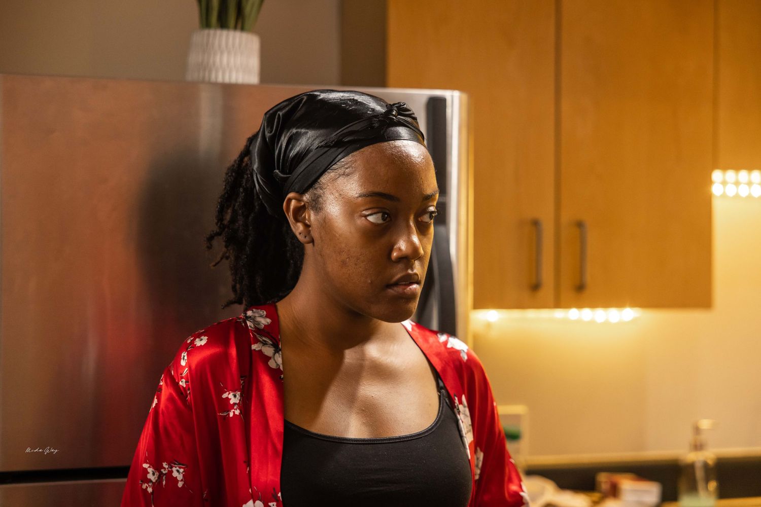 Person in red jacket sits in warmly lit kitchen setting.