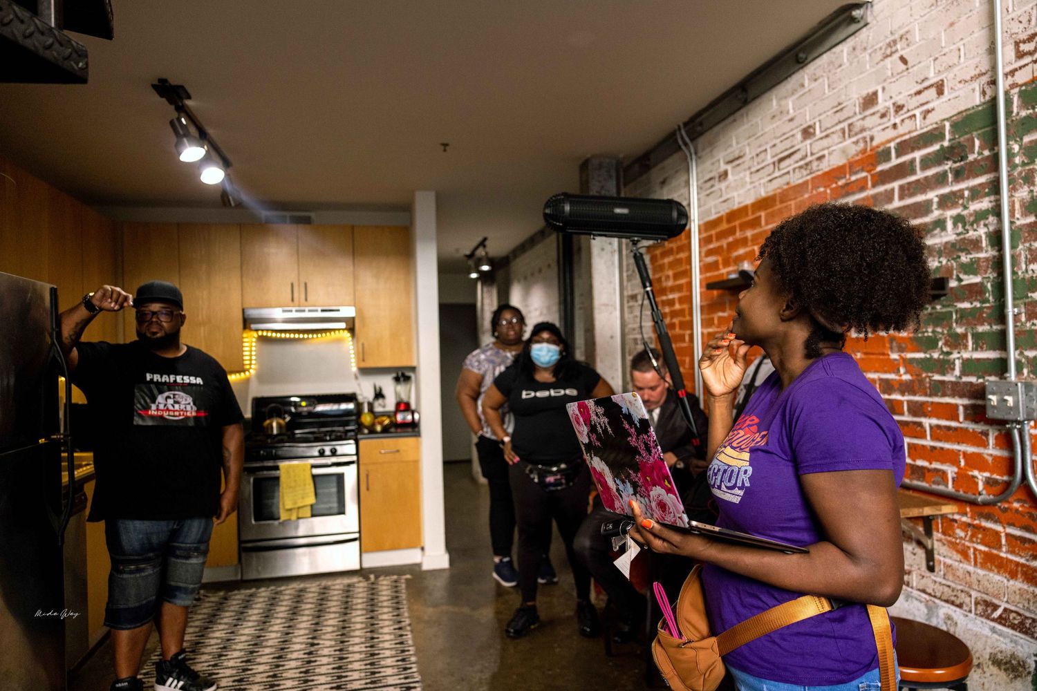 Group gathered in industrial-style kitchen with exposed brick walls.