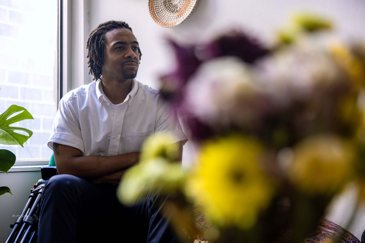 Person in white shirt sitting by window with blurred yellow flowers in foreground.
