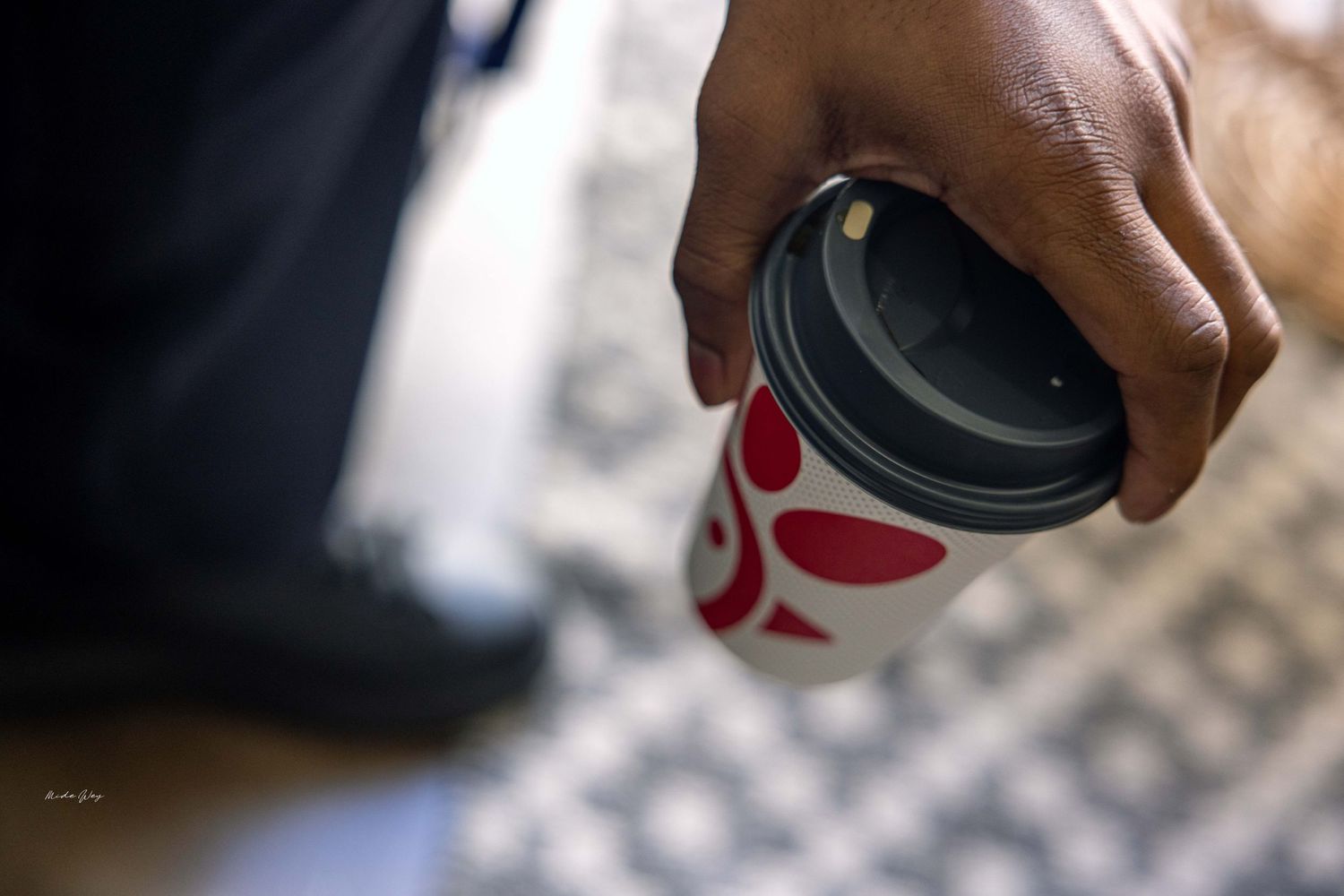 Close-up of a hand holding a disposable coffee cup with red branding.