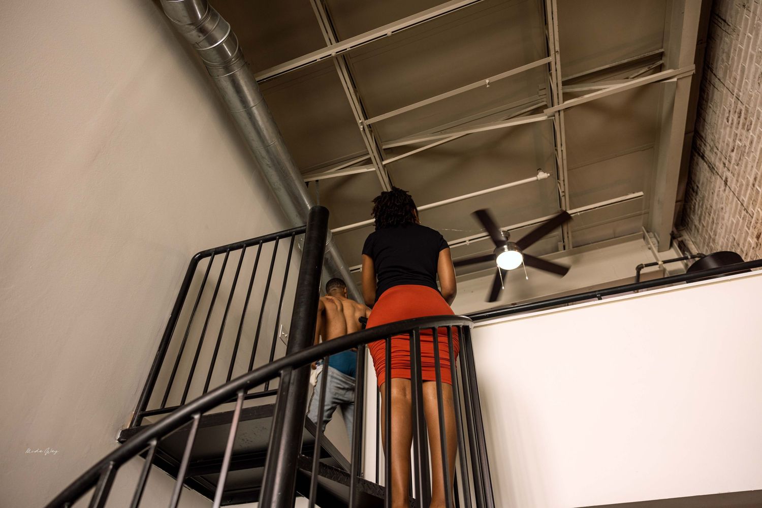 Low-angle view of someone ascending a black spiral staircase against an industrial ceiling.