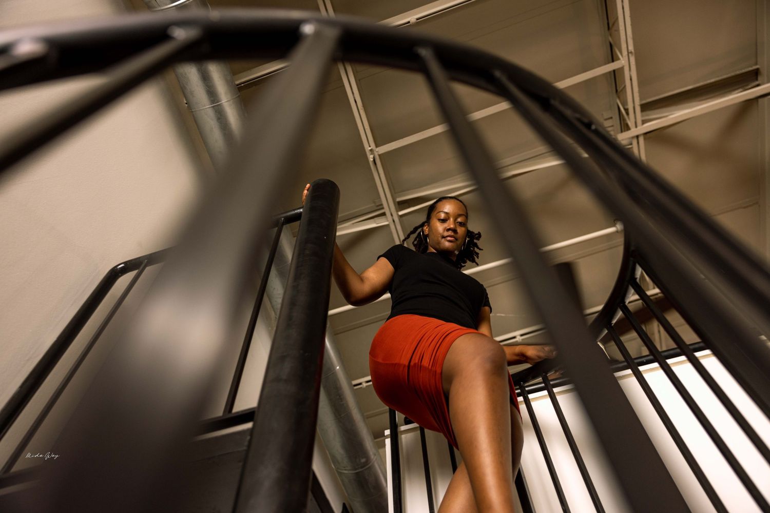 Figure climbing a modern spiral staircase wearing a black top and red shorts.