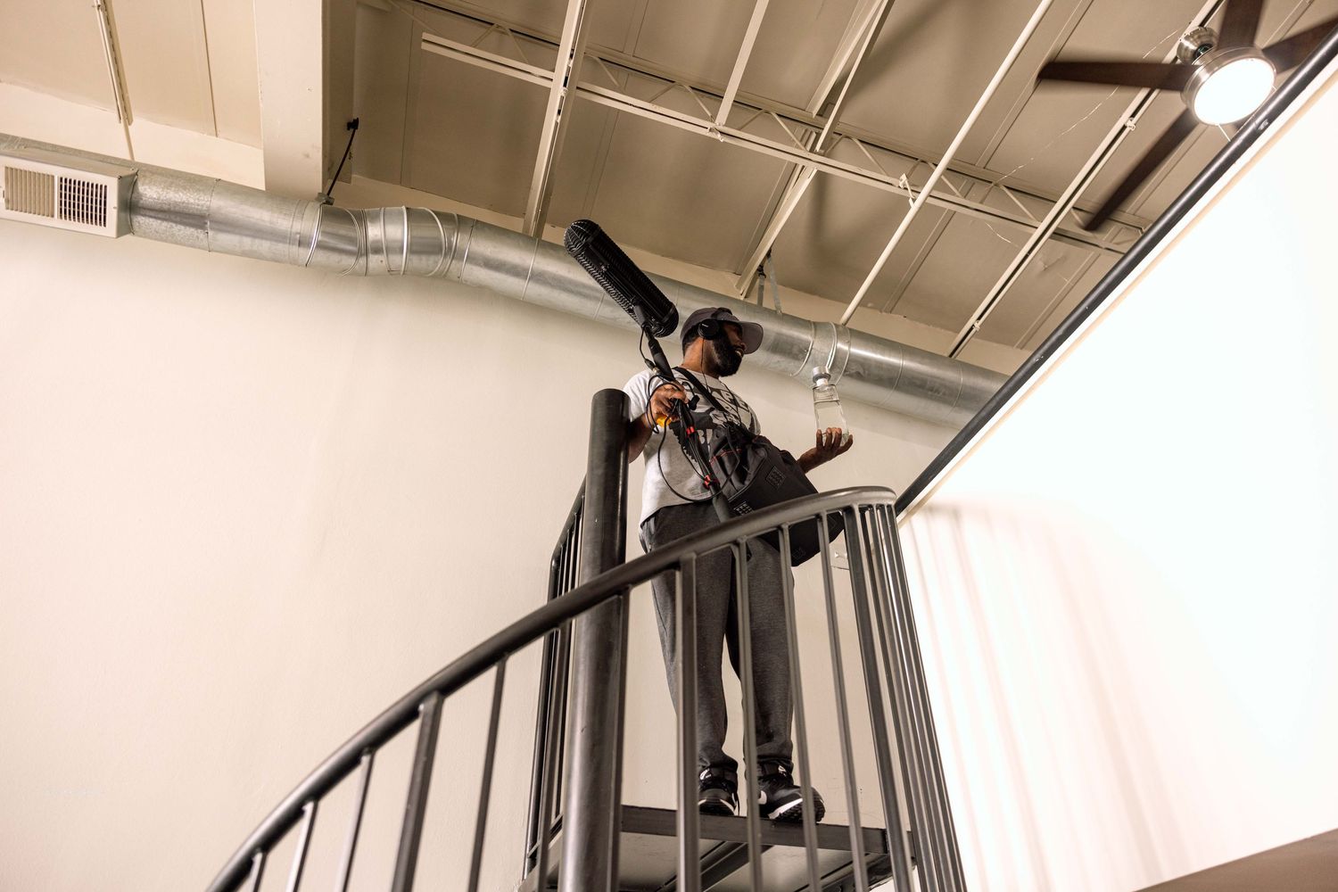 A person in black clothing stands at the top of a spiral metal staircase with industrial exposed ceiling.