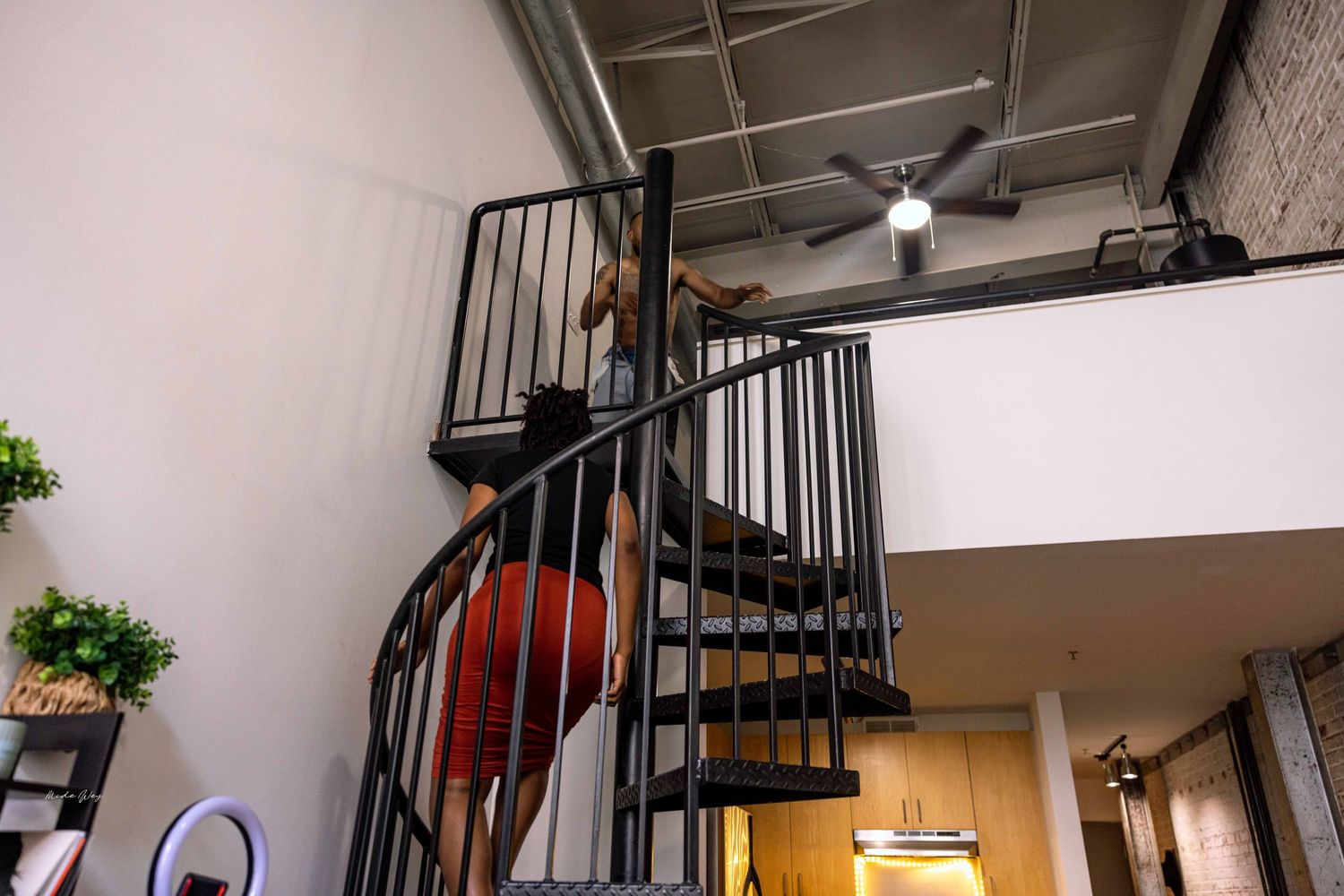 A spiral staircase leads upward in an industrial-style space with exposed brick walls and ceiling.