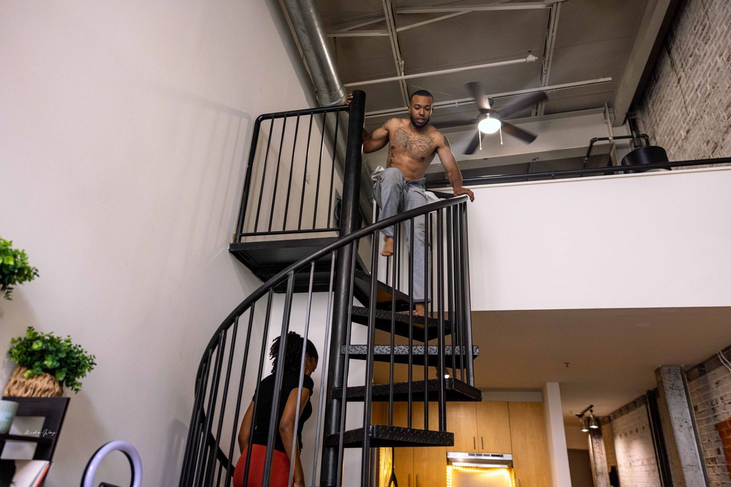 People ascending a black spiral staircase in an industrial-style loft space.