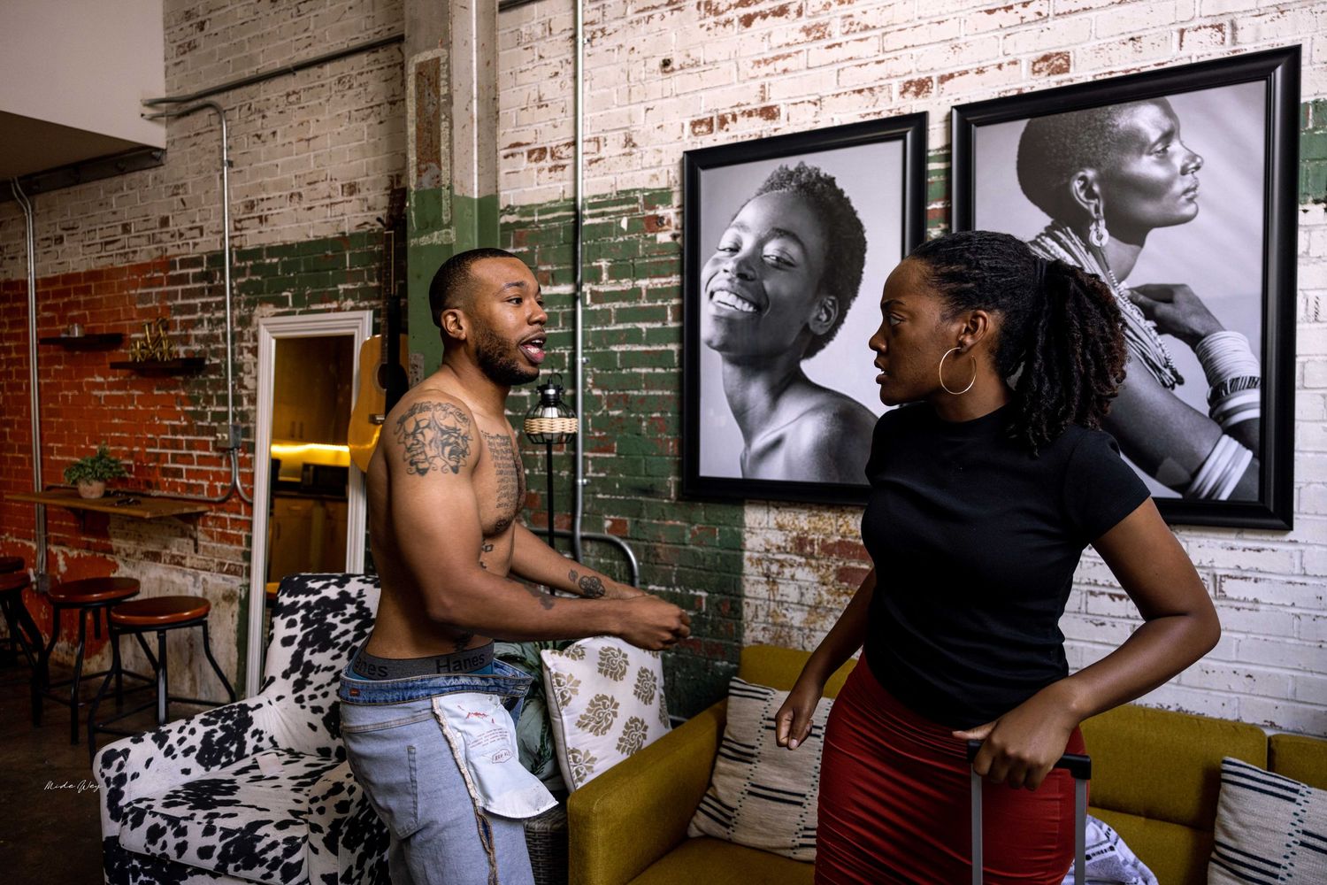 A conversation takes place in front of vintage black and white portraits mounted on exposed brick.