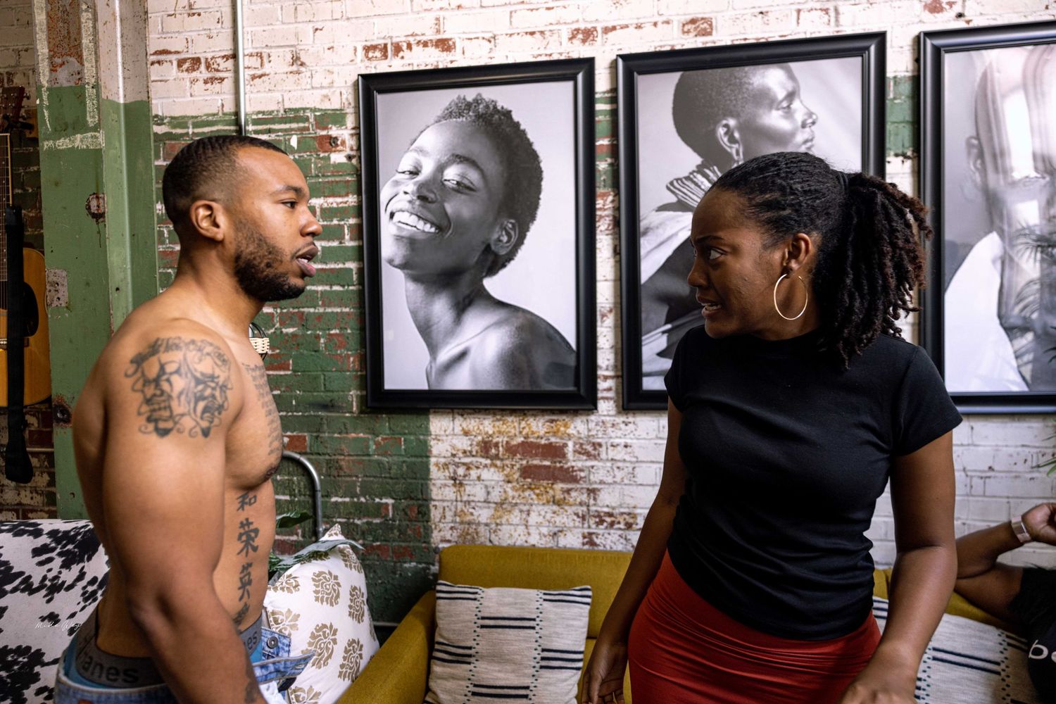Two people having a discussion in front of striking black and white portrait photographs on brick wall.