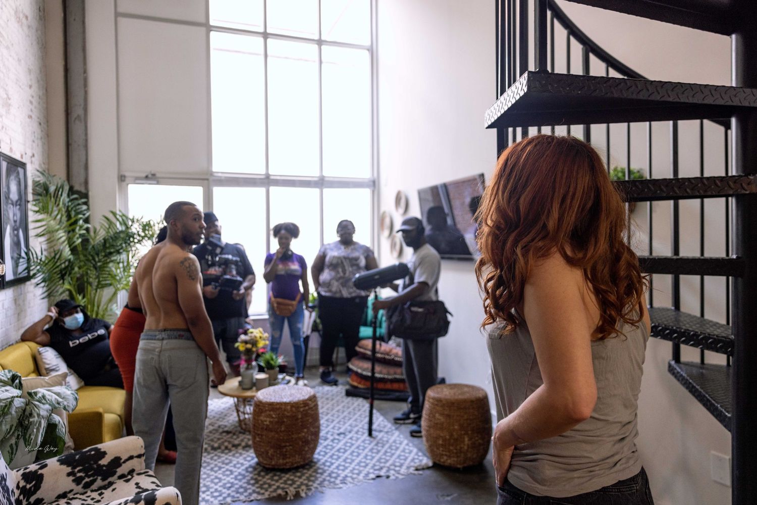 People socializing in a modern loft space with spiral staircase and decorative wall portraits.