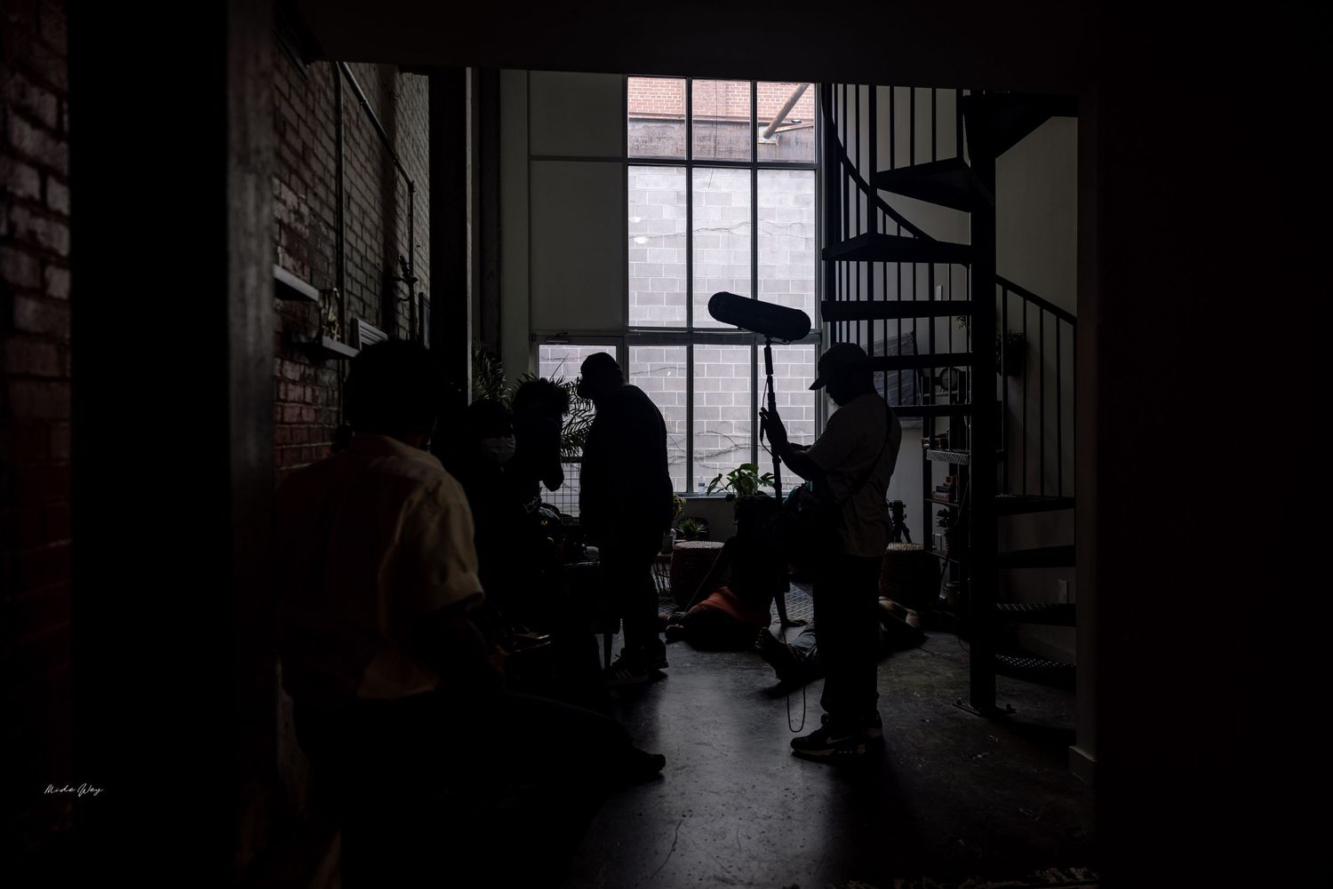 Silhouettes of people working in a dark interior space with spiral staircase and window light.