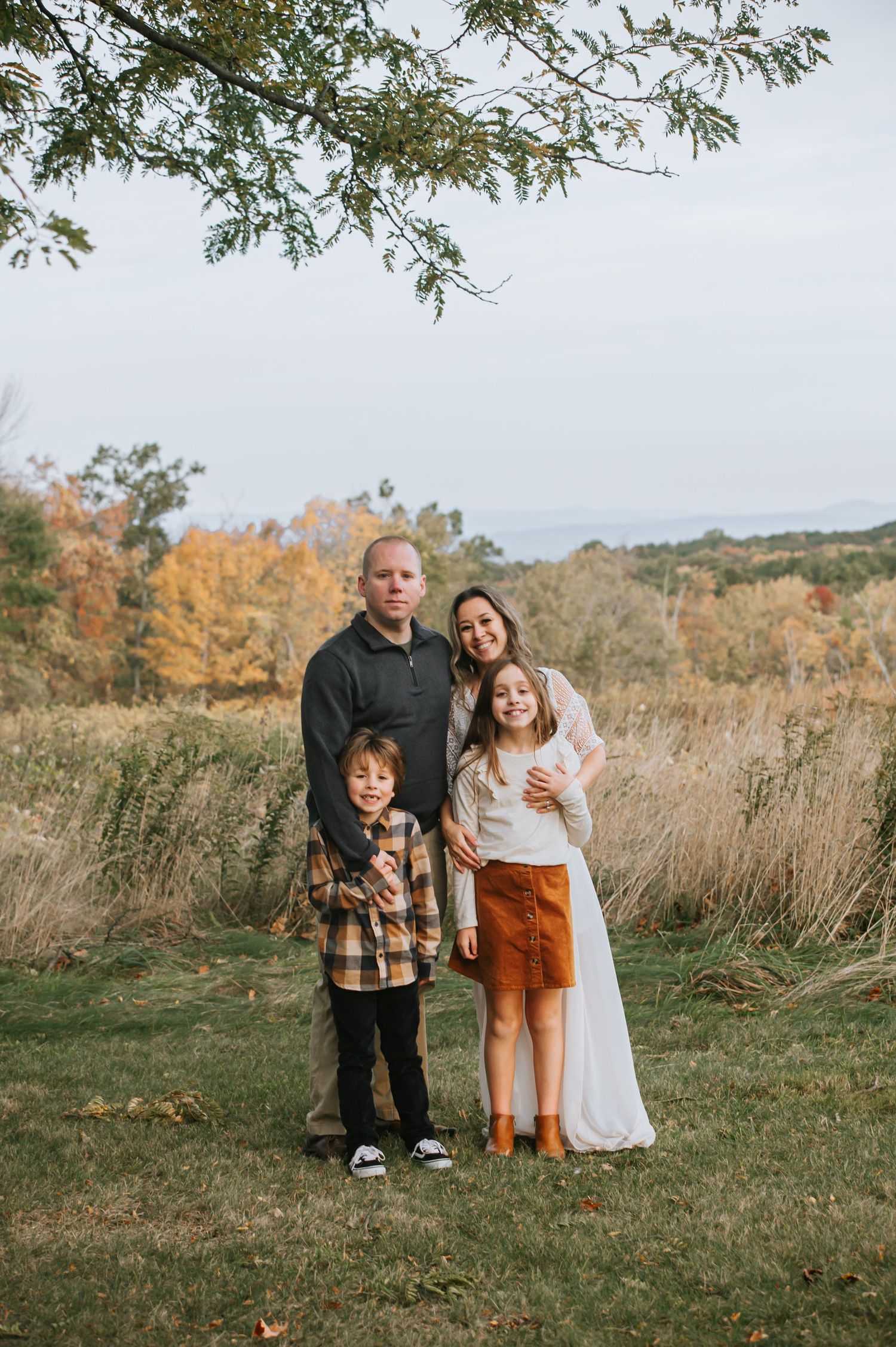 Family of four poses together in an autumn field with tall grass and trees in the background.