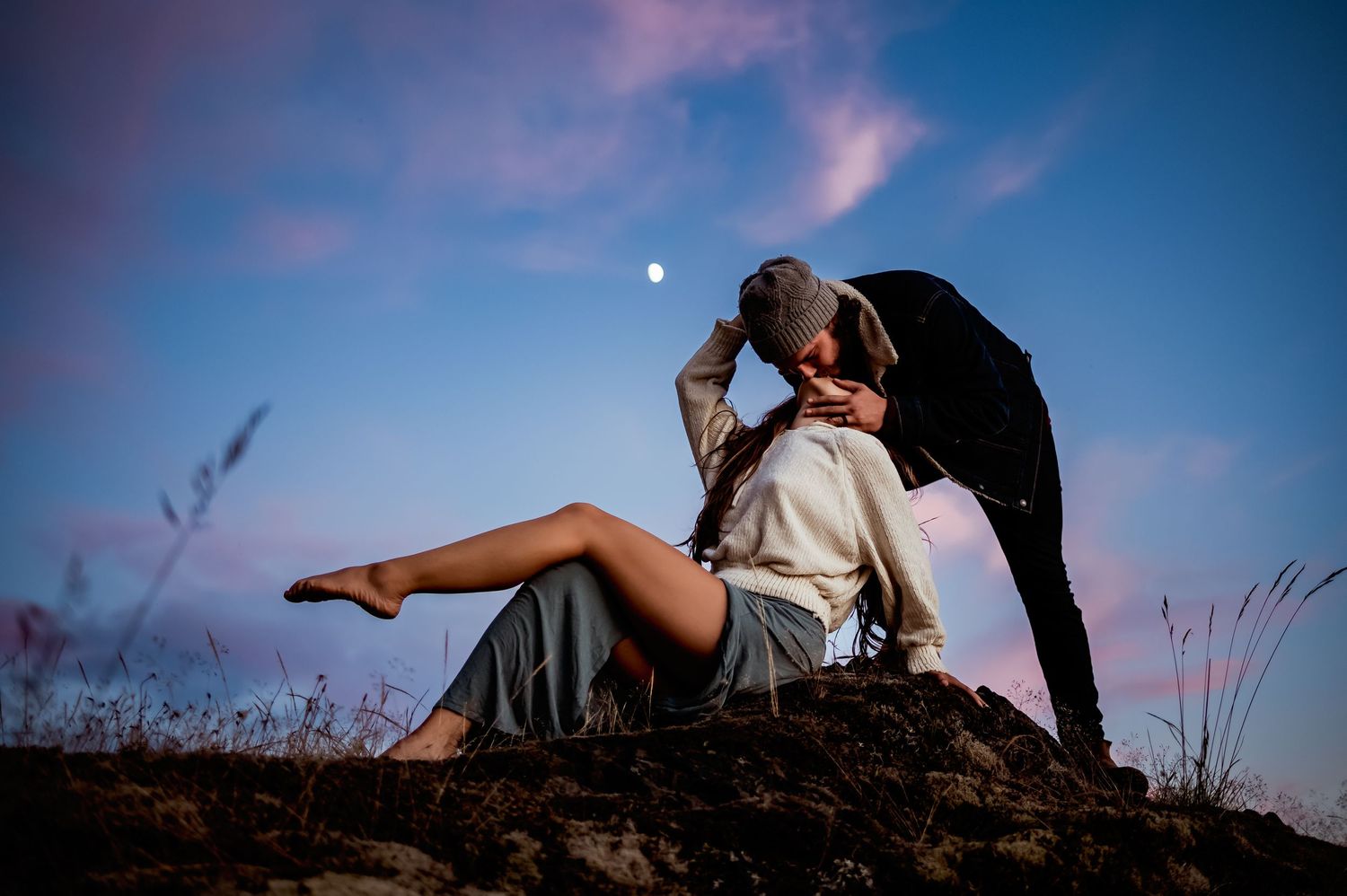 Silhouetted figures embrace against dramatic twilight sky with moon.