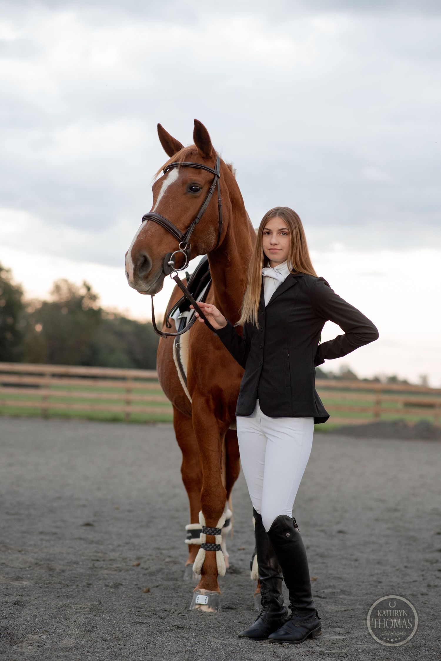 Elegant equestrian rider in formal riding attire poses with a chestnut horse in an outdoor arena.