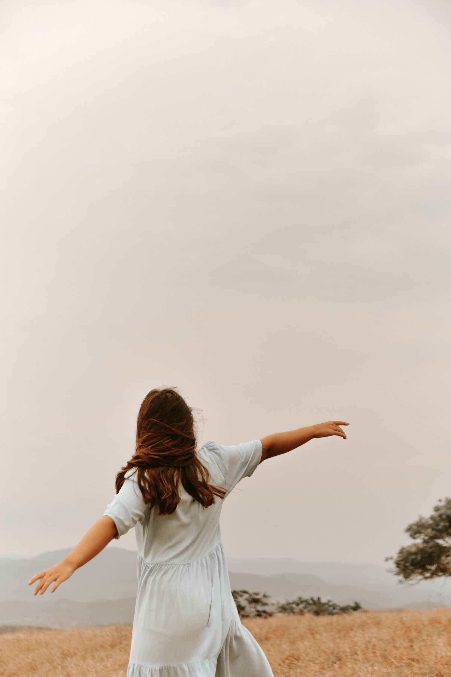 A person in a flowing white dress spins with arms outstretched in a golden field.
