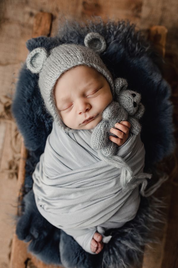 Eden Prairie newborn photographer | baby-wrapped-in-blue-wrap-with-blue-knitted-bear-bonnet-on-blue-fur-on-wooden floor