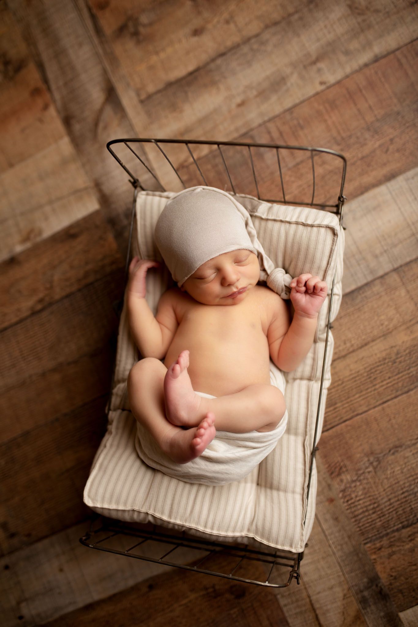 Eden Prairie newborn photographer | newborn-laying-on-a-wire-bed-wearing-a-tan-sleepy-cap-all-on-top-of-wooden-backdrop