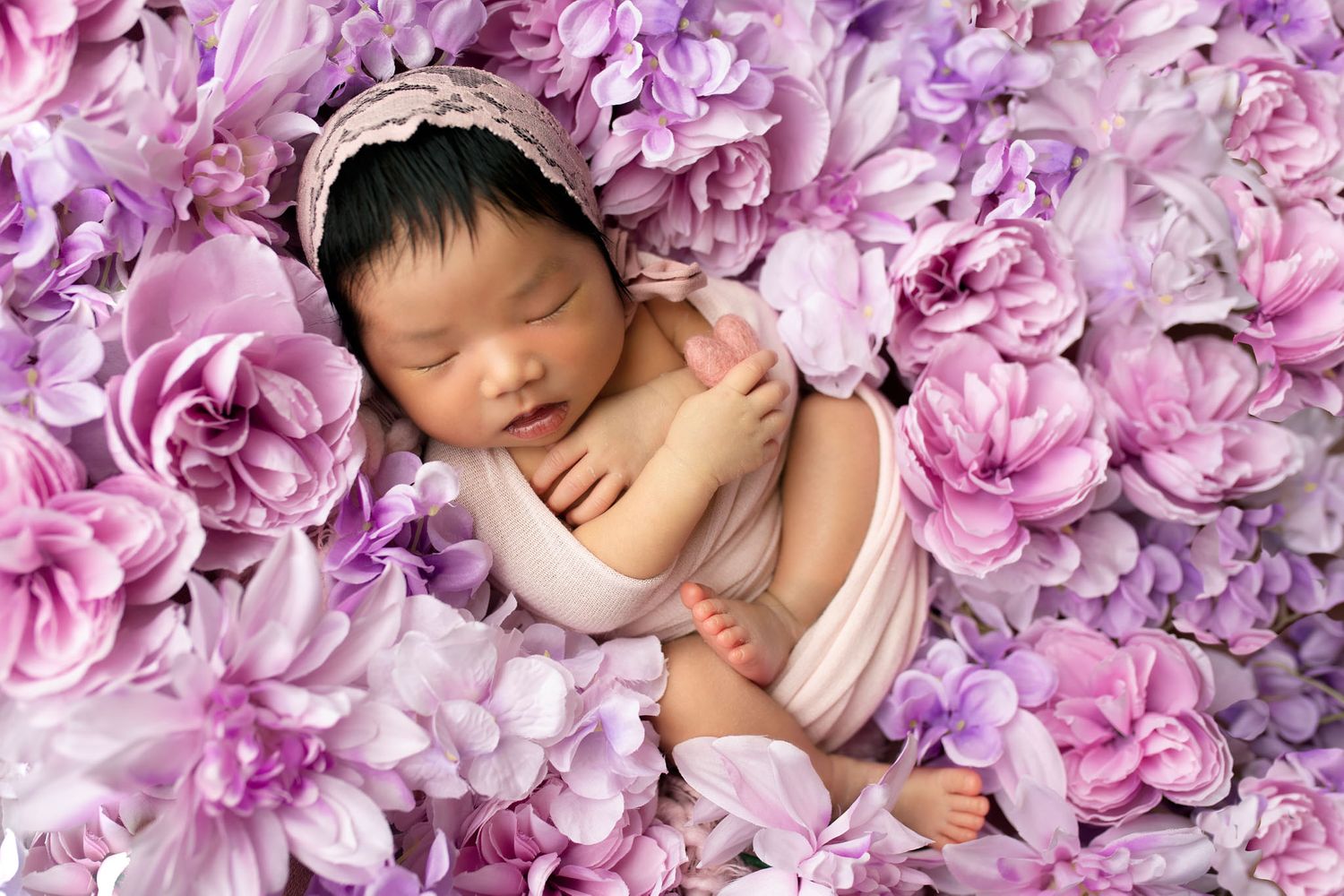 Eden Prairie newborn photographer | newborn-girl-wrapped-in-pink-bonnet-sitting-upright-in-pink-purple-white-flowers