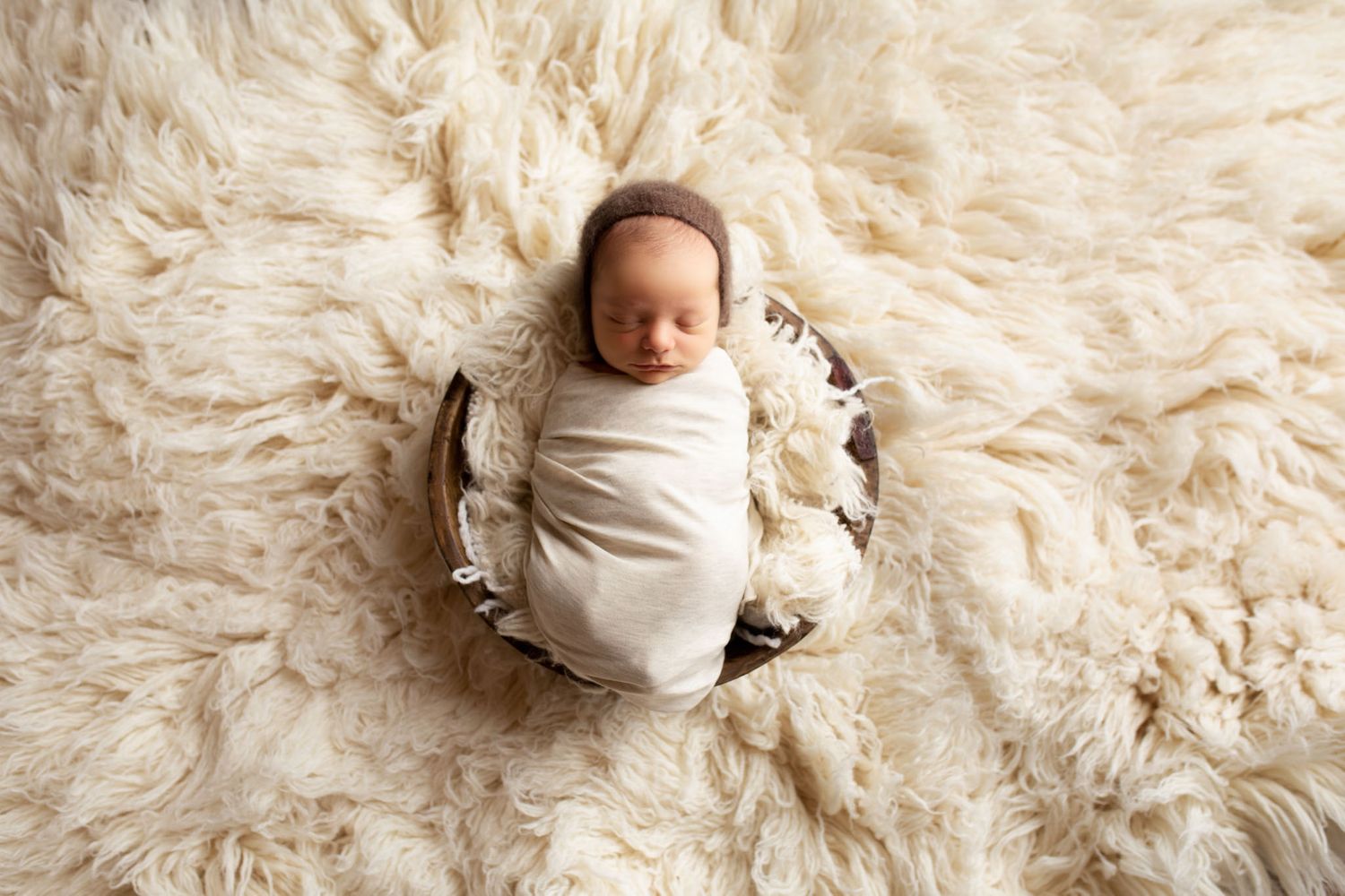 Eden Prairie newborn photographer | newborn-on-small-cream-fur-in-wood-bowl-on-cream-rug-baby-in-cream-wrap-bonnet-on