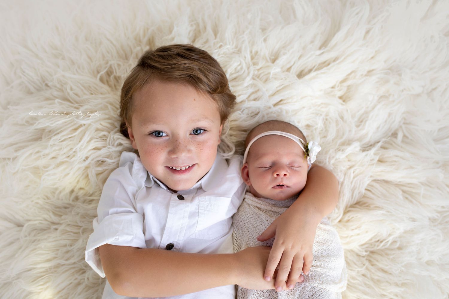 Eden Prairie newborn photographer | newborn wrapped-in-white-wrap-with-white-bow-laying-on-cream rug brother holding her