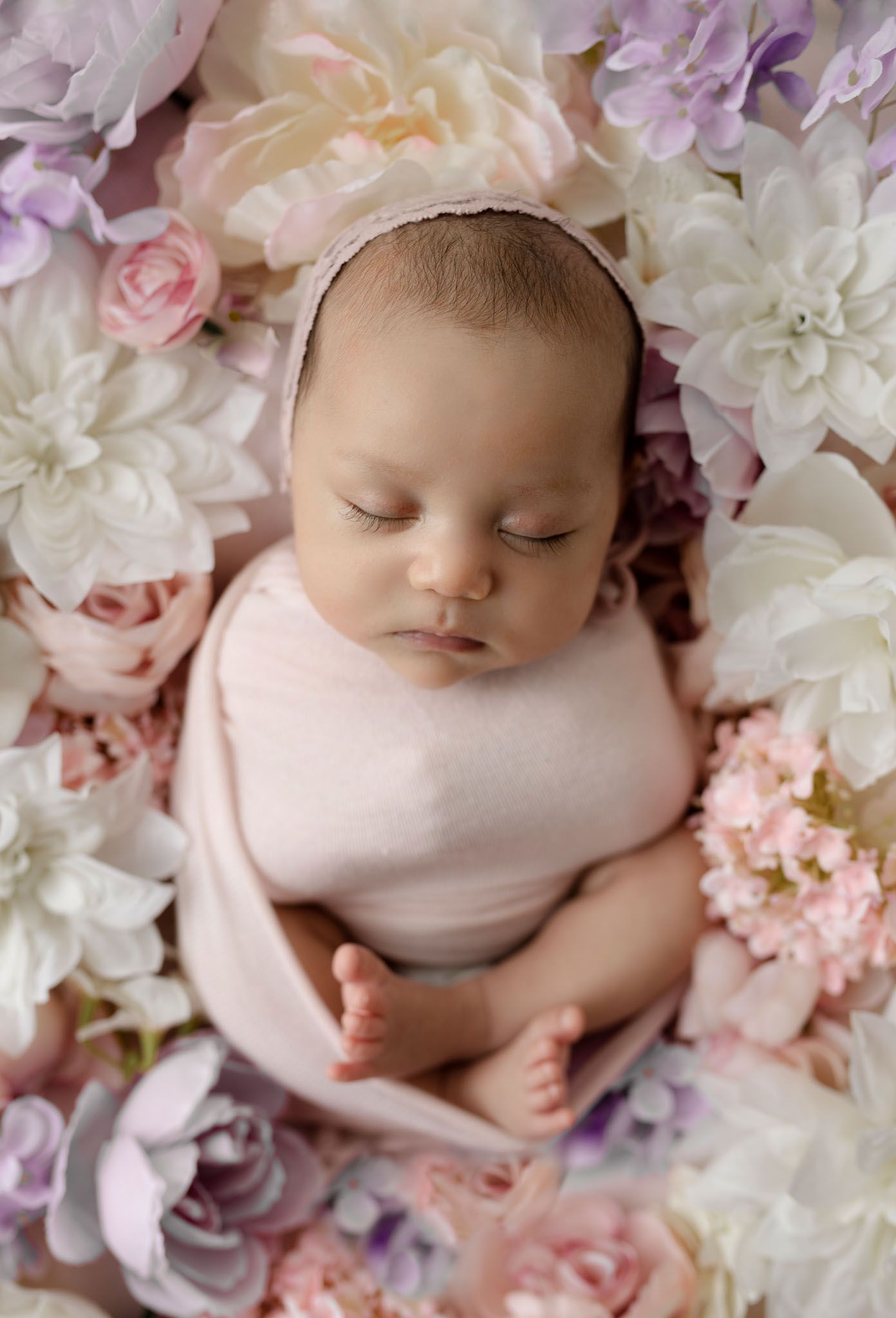 Eden Prairie newborn photographer | newborn-girl-wrapped-in-pink-wrap-pink-bonnet-sitting-in-pink-purple-white-flowers