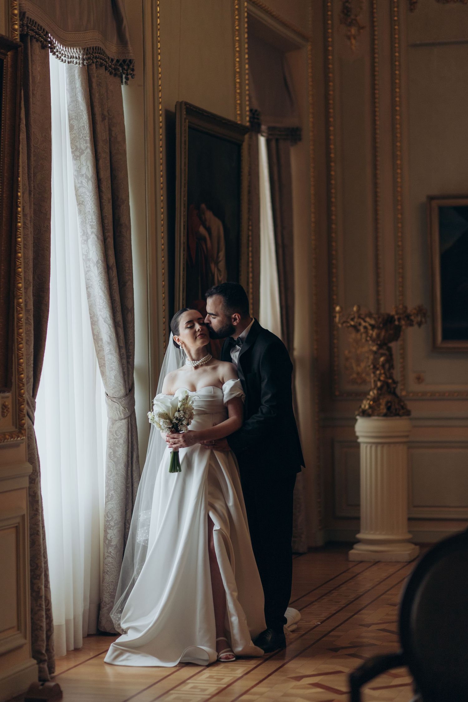 An intimate moment shared in an ornate room with golden details and tall windows.