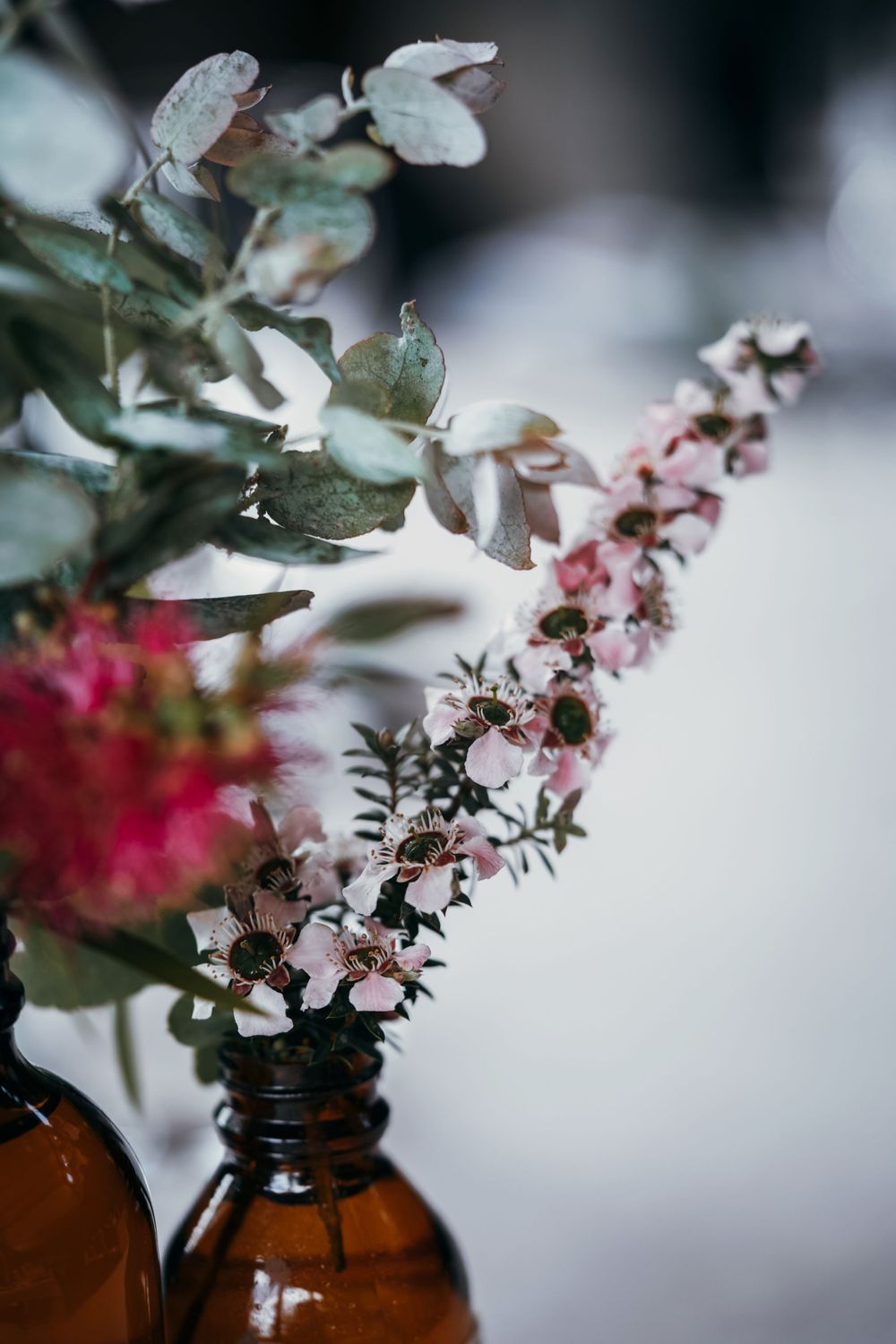 Close-up of delicate pink and white flowers in amber glass bottle with soft focus background.