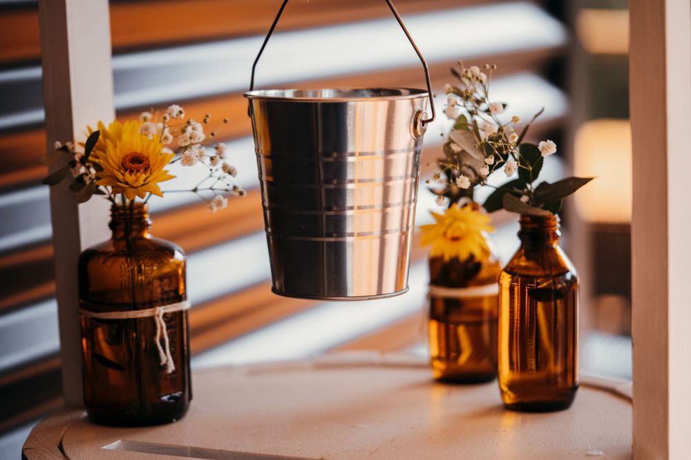 Rustic arrangement of sunflowers in amber bottles with hanging metal bucket decoration.