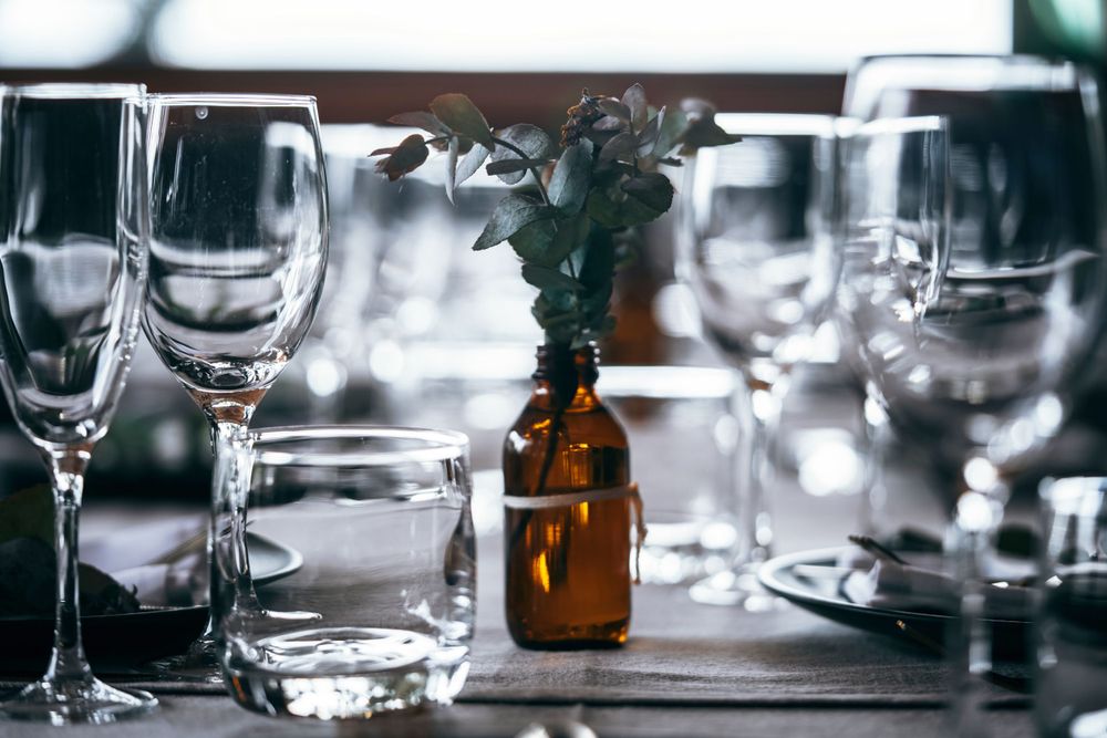 Table setting with wine glasses and amber bottle vase in moody lighting.