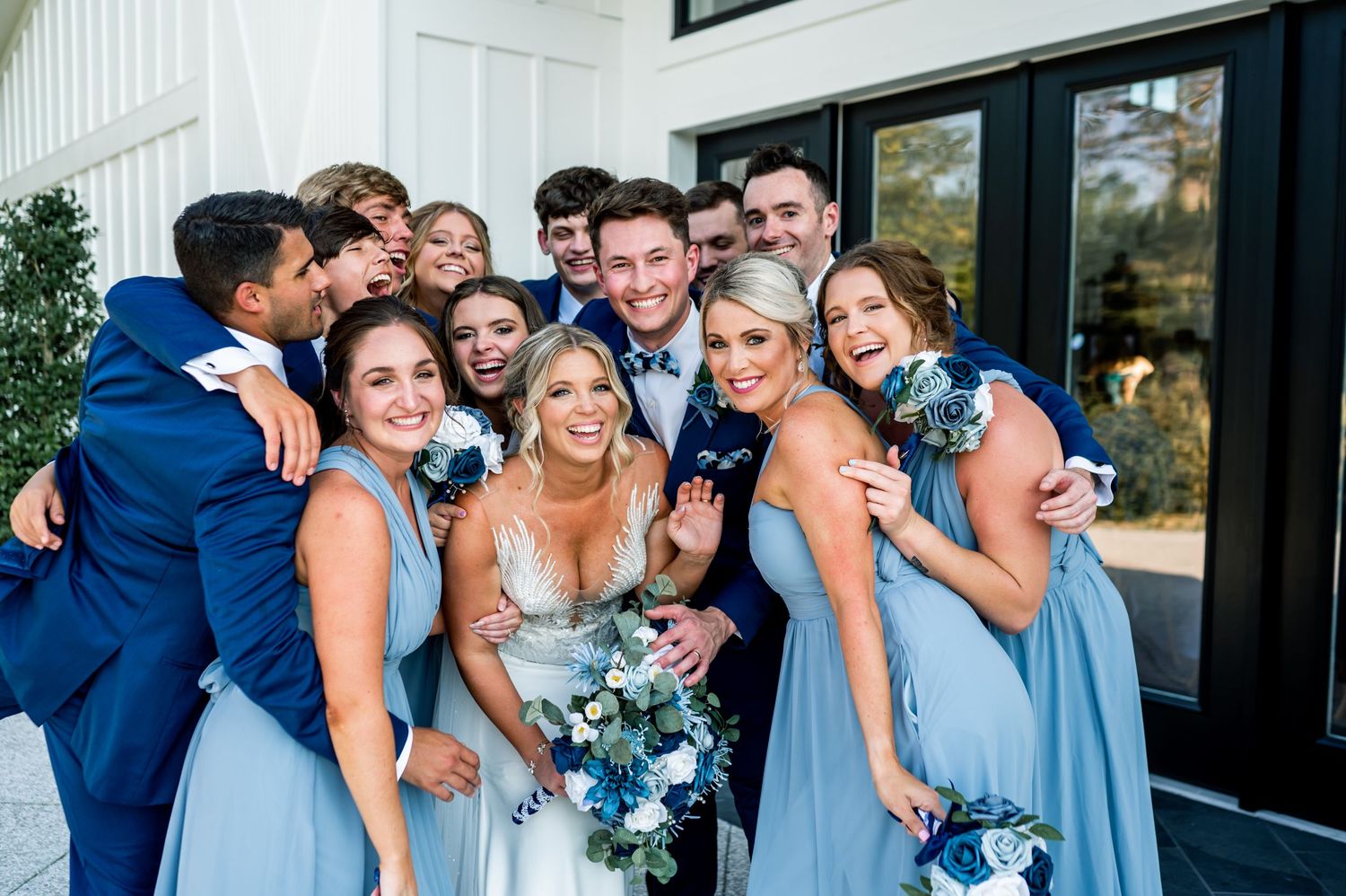 Wedding party poses casually outside modern white venue with black trim.