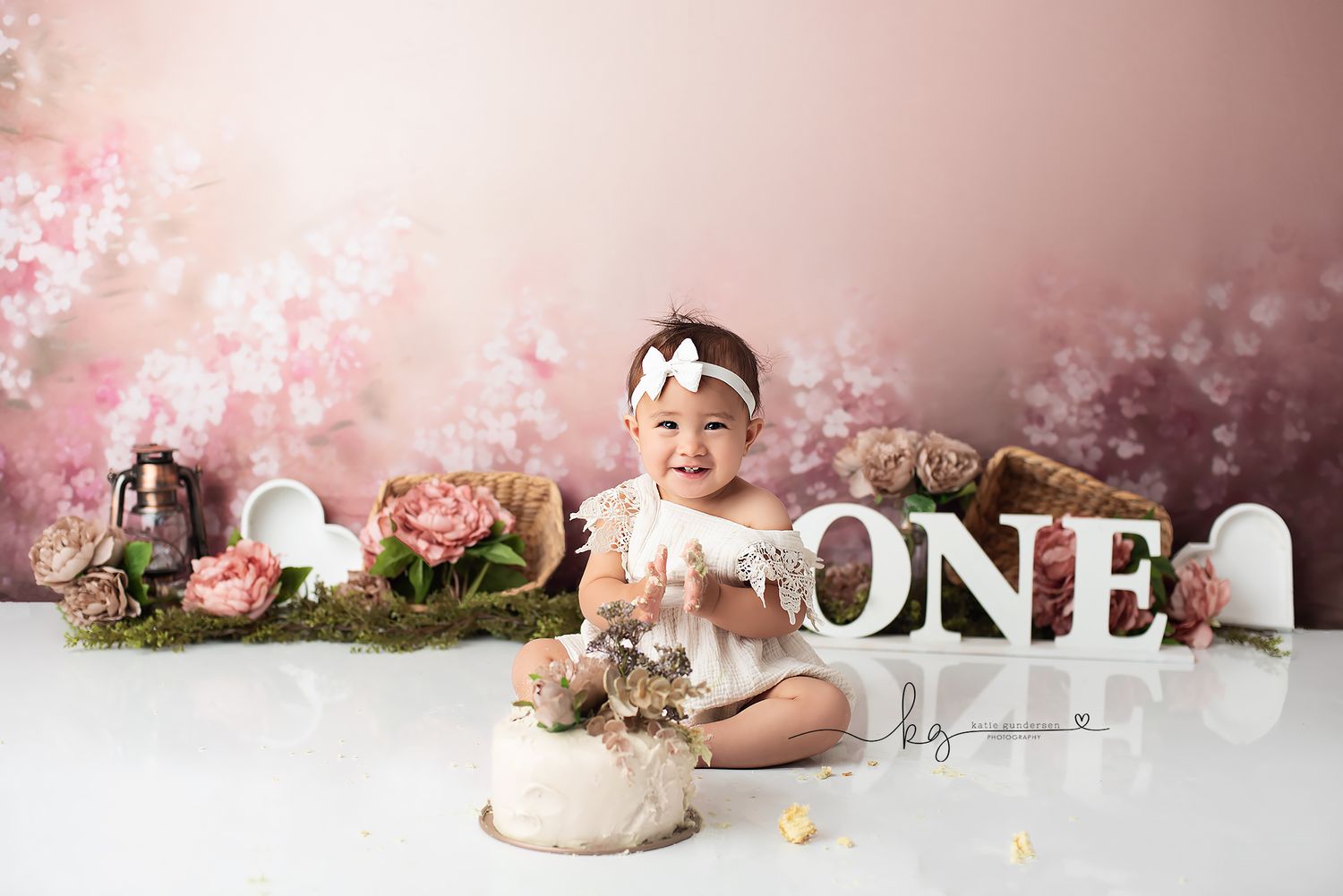 First birthday celebration setup with pink floral backdrop and 'ONE' lettering with cake smash props.