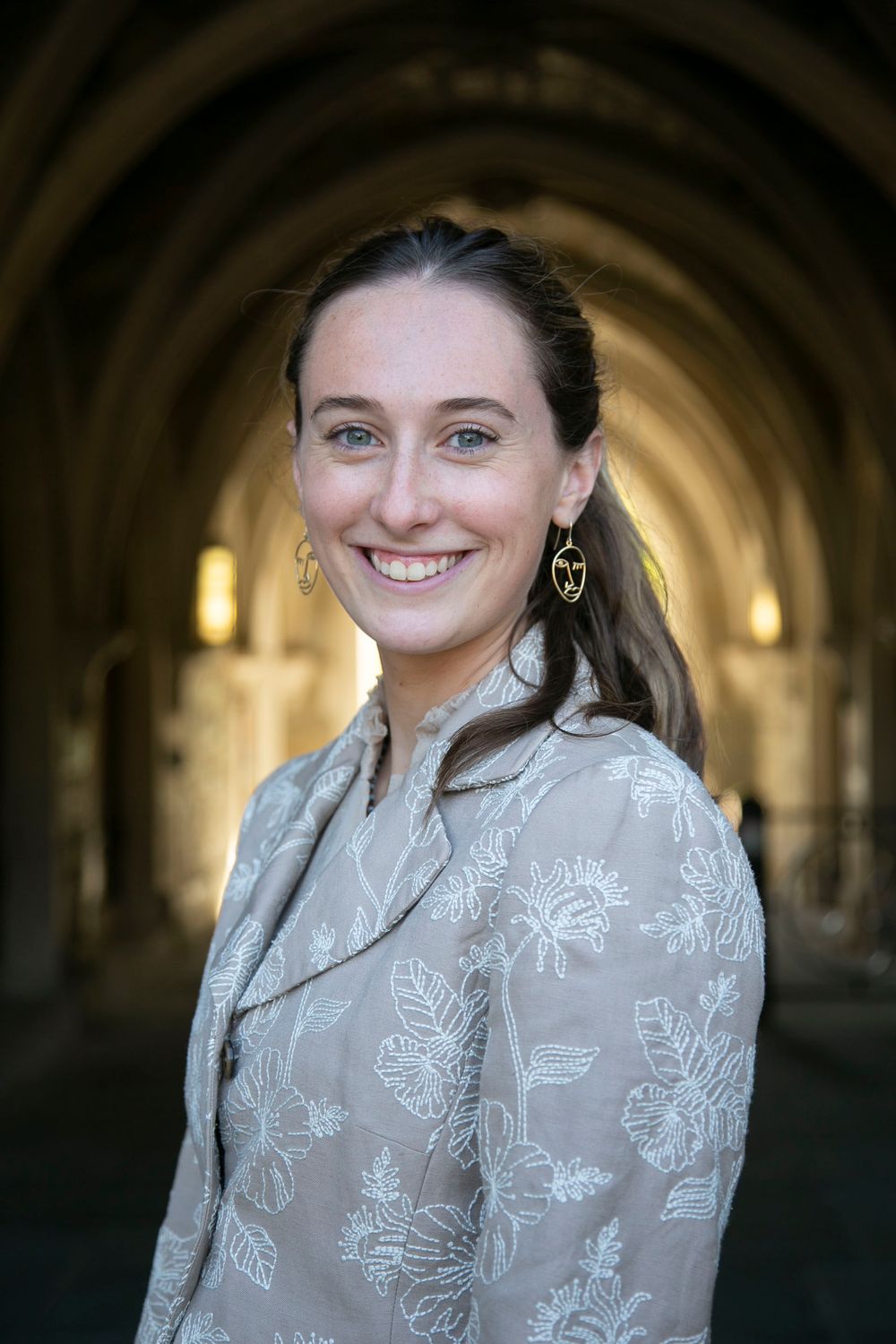 Smiling young woman in floral blouse posing under stone archway.