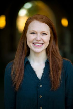 Smiling redhead woman with long hair wearing dark teal button-up shirt outdoors.