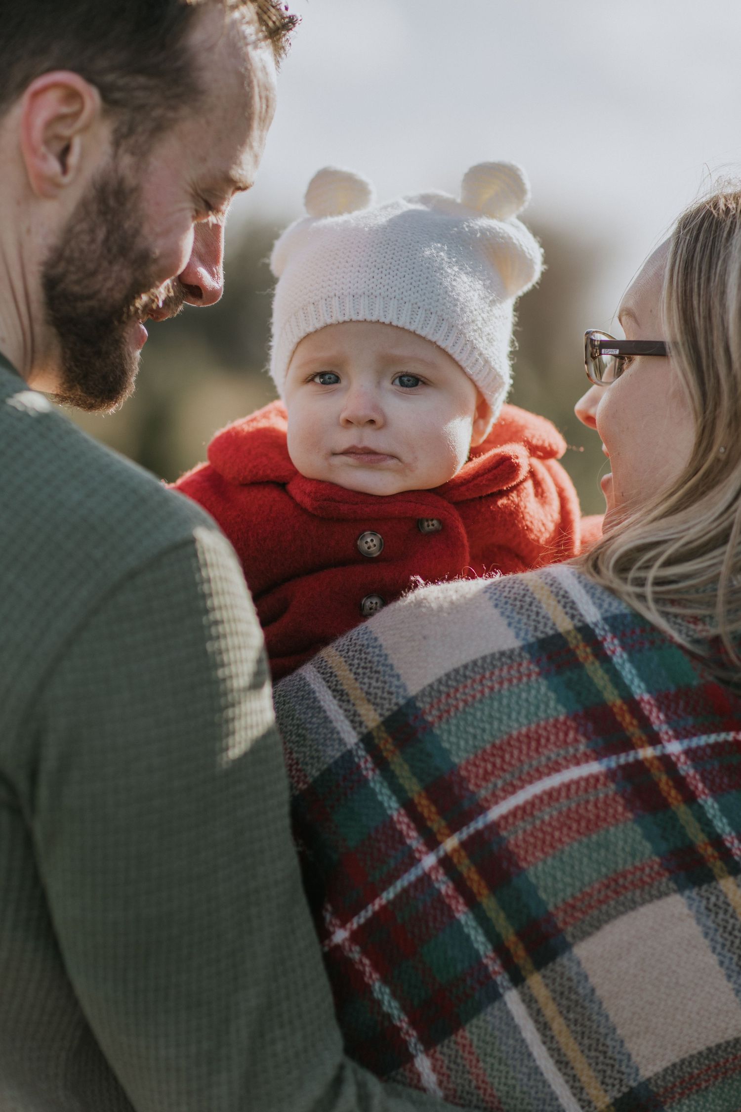 Family cuddling together wrapped in plaid blanket during winter photo session.
