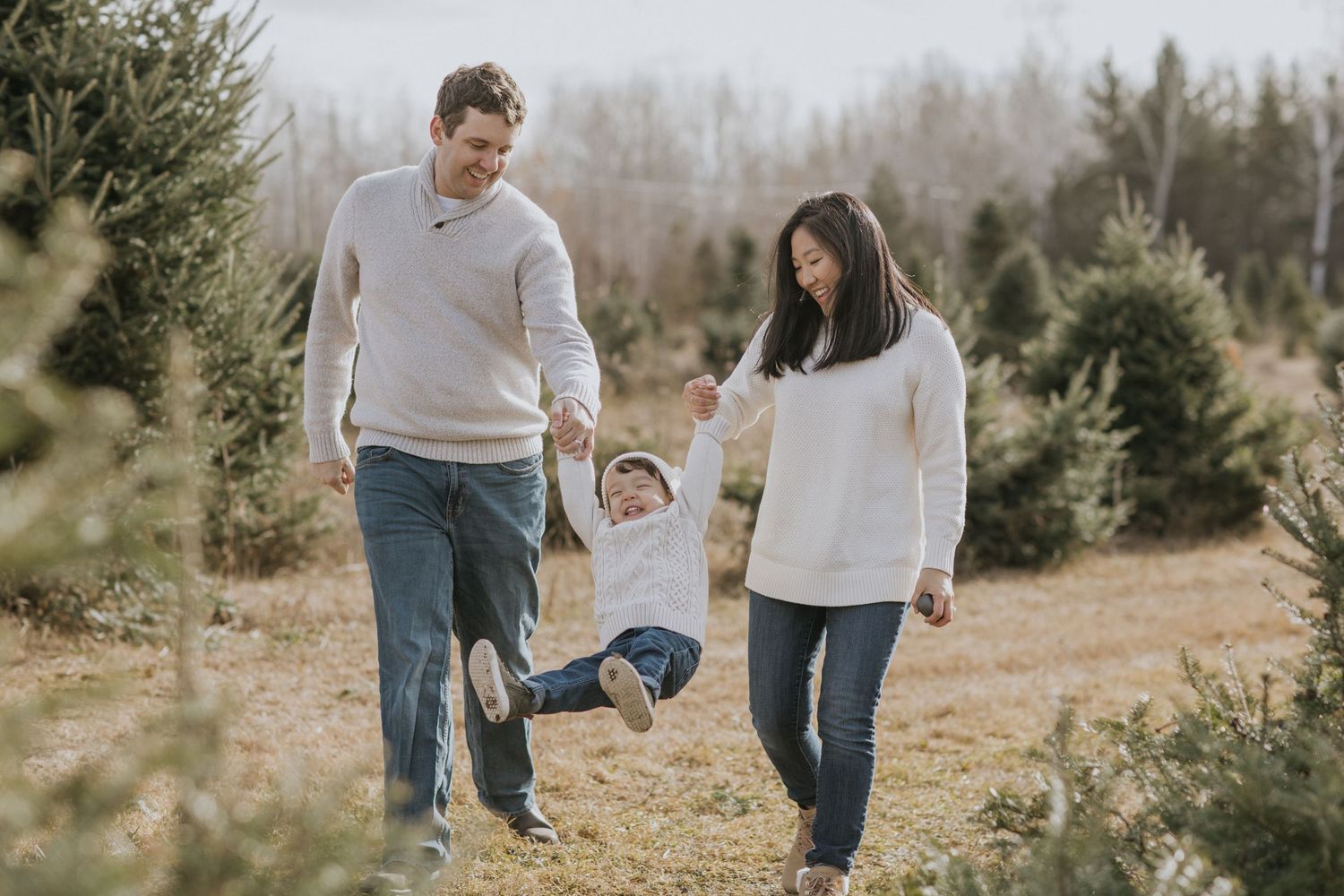 Family walking together through evergreen tree farm in casual winter attire.
