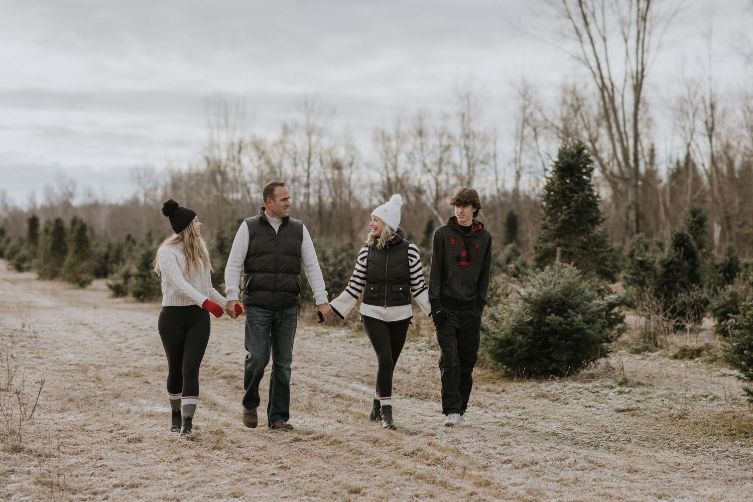 Family walking together through a rustic field with evergreen trees in the background.