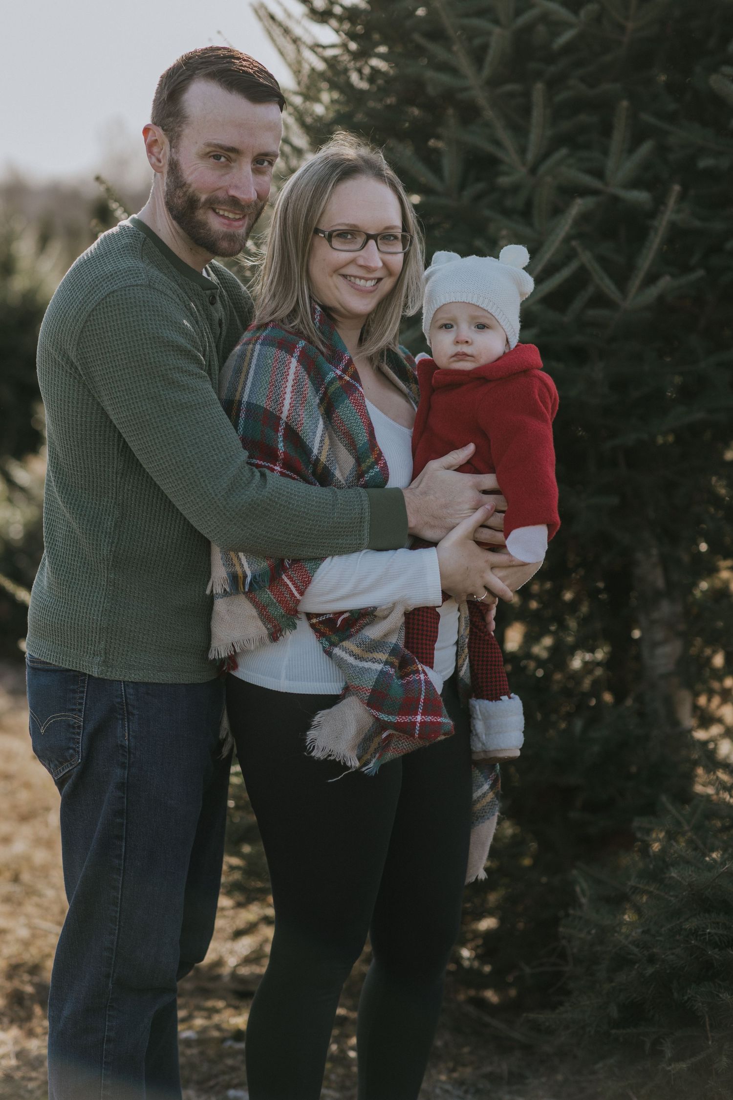 Family posing together by evergreen trees in winter clothing with small baby.
