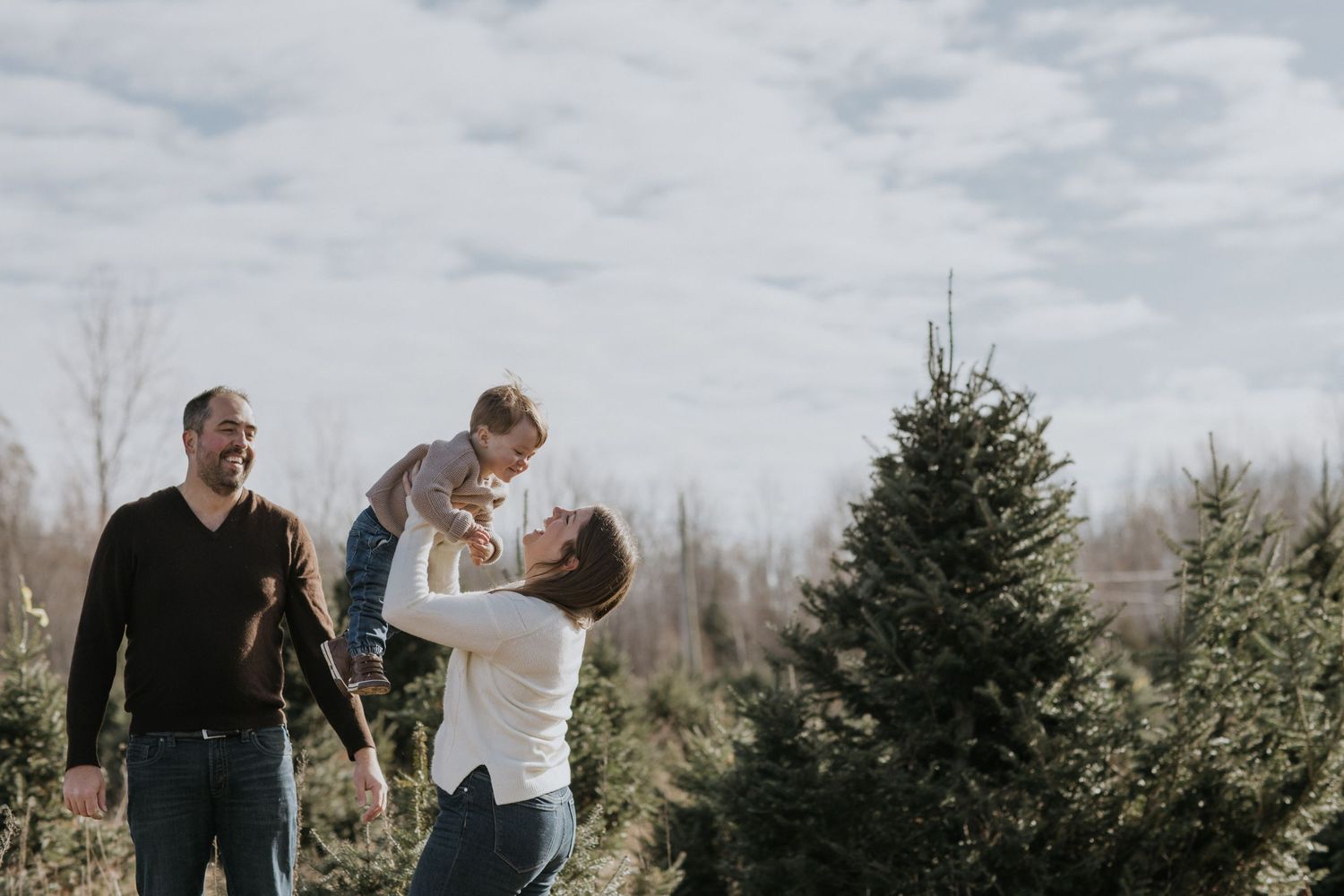 Winter family photoshoot among evergreen trees with overcast sky.