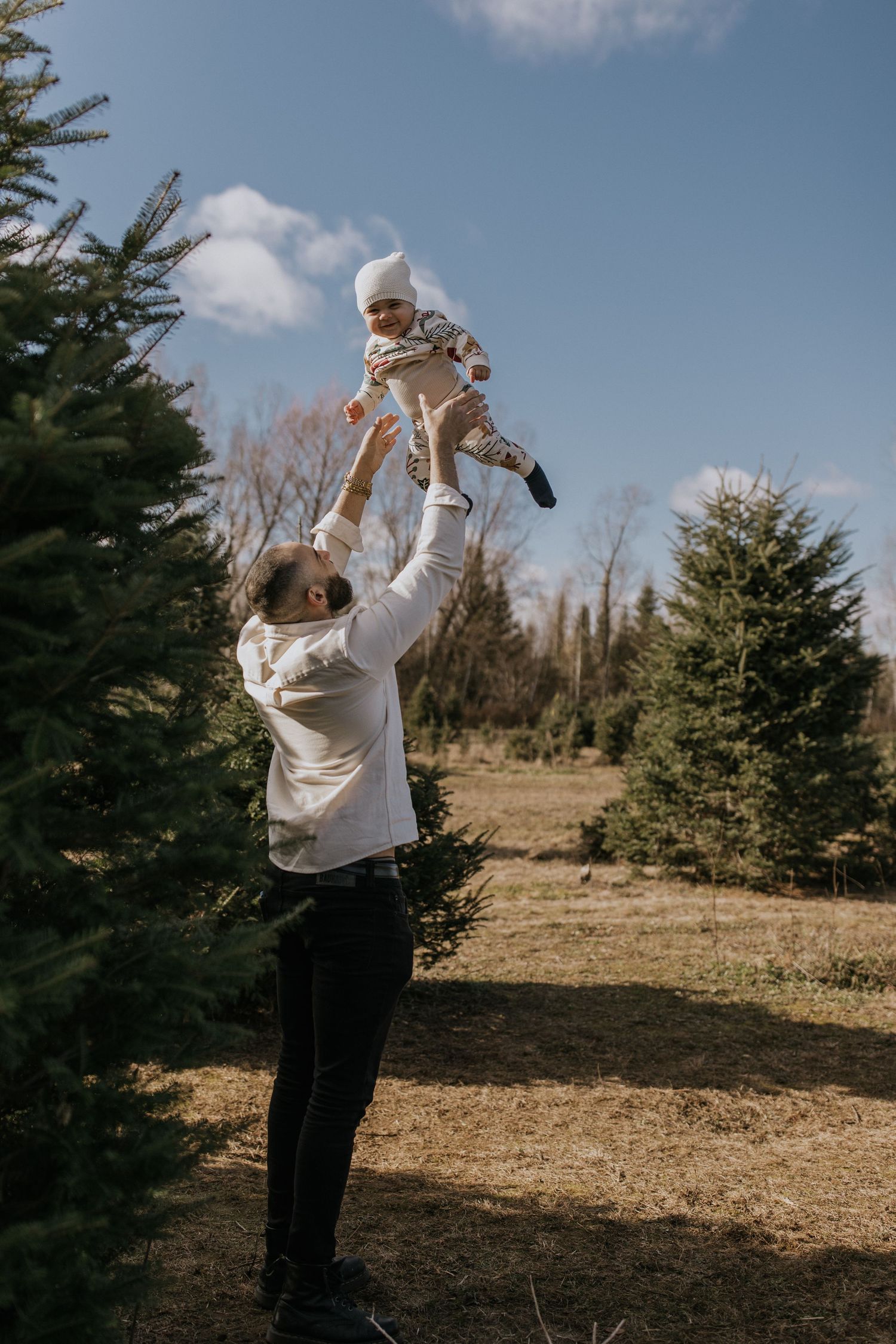 Playful outdoor portraits with evergreen trees and blue sky backdrop.