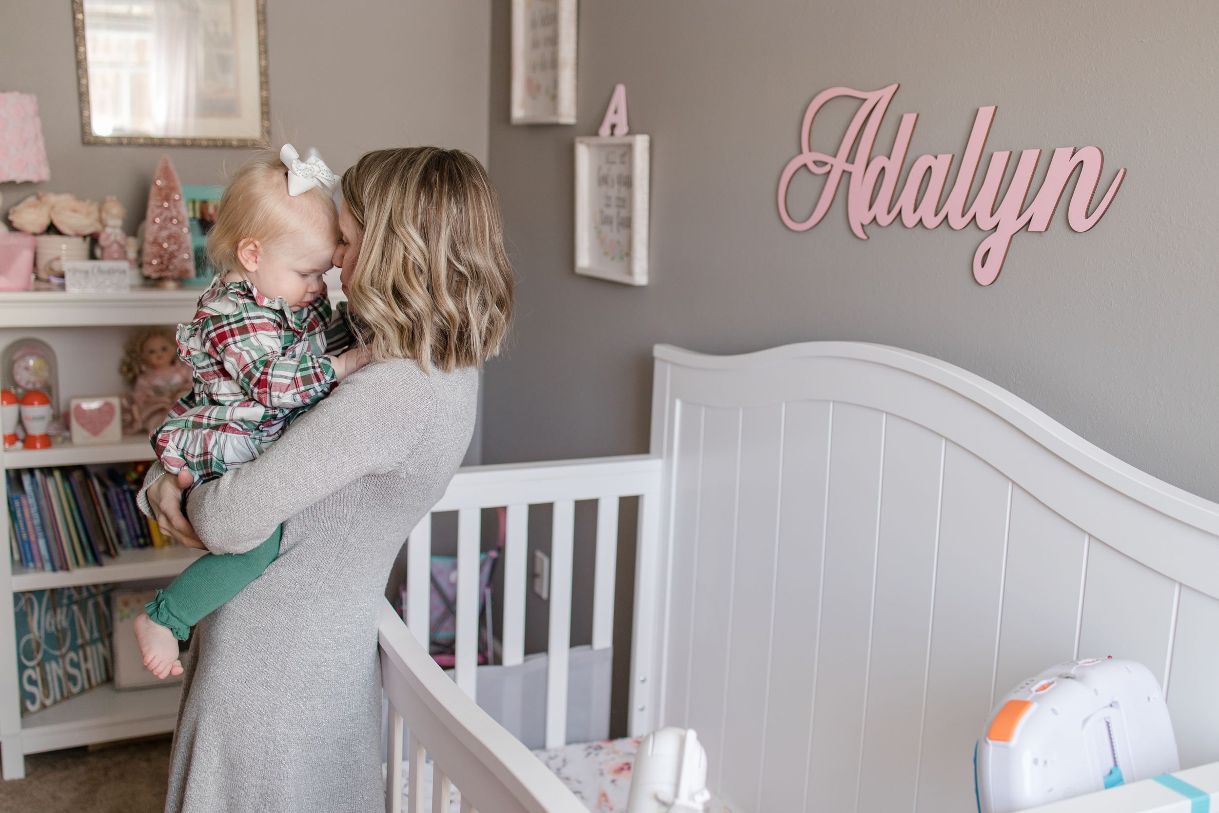 A cozy nursery room decorated in soft grays and whites with the name 'Adalyn' displayed on the wall.