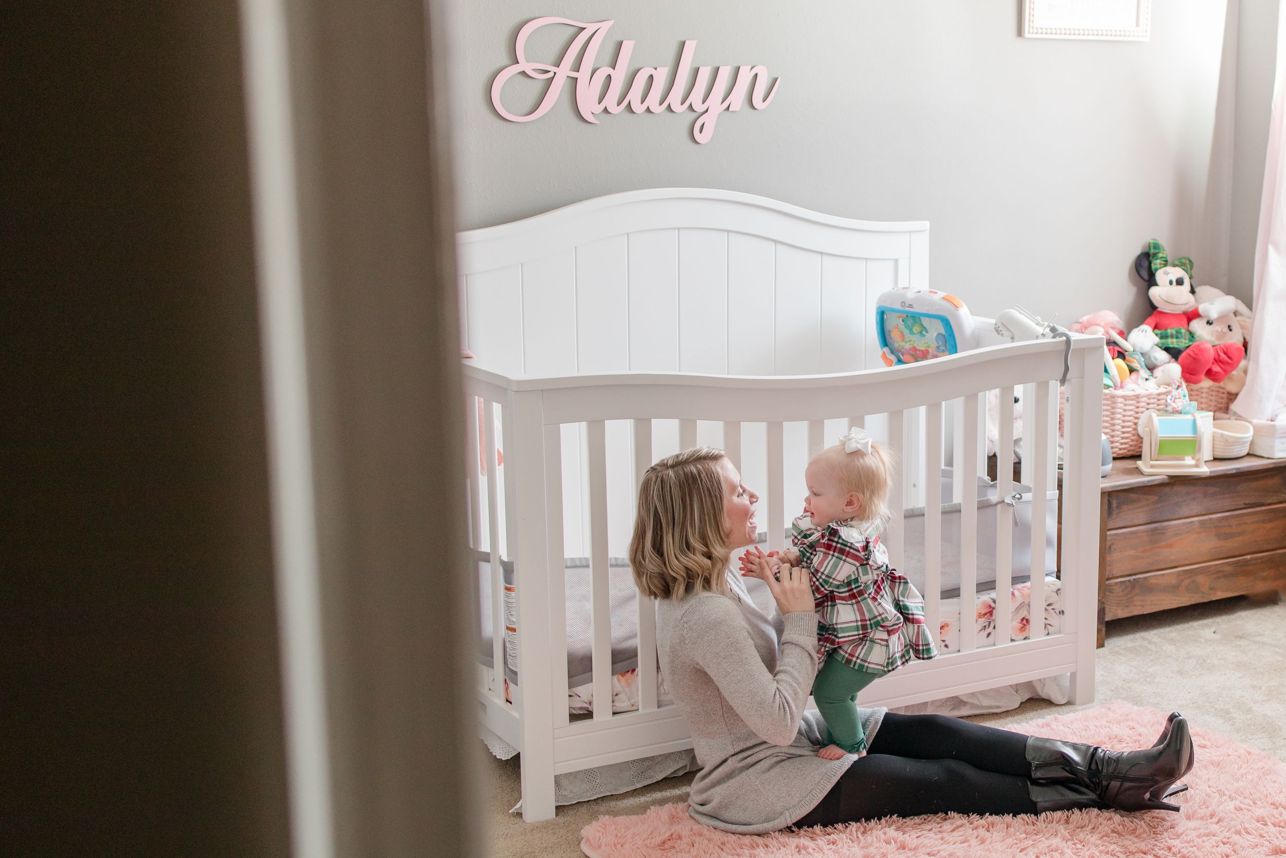 A tender nursery scene showing a quiet moment by a white crib with the name 'Adalyn' on the wall.