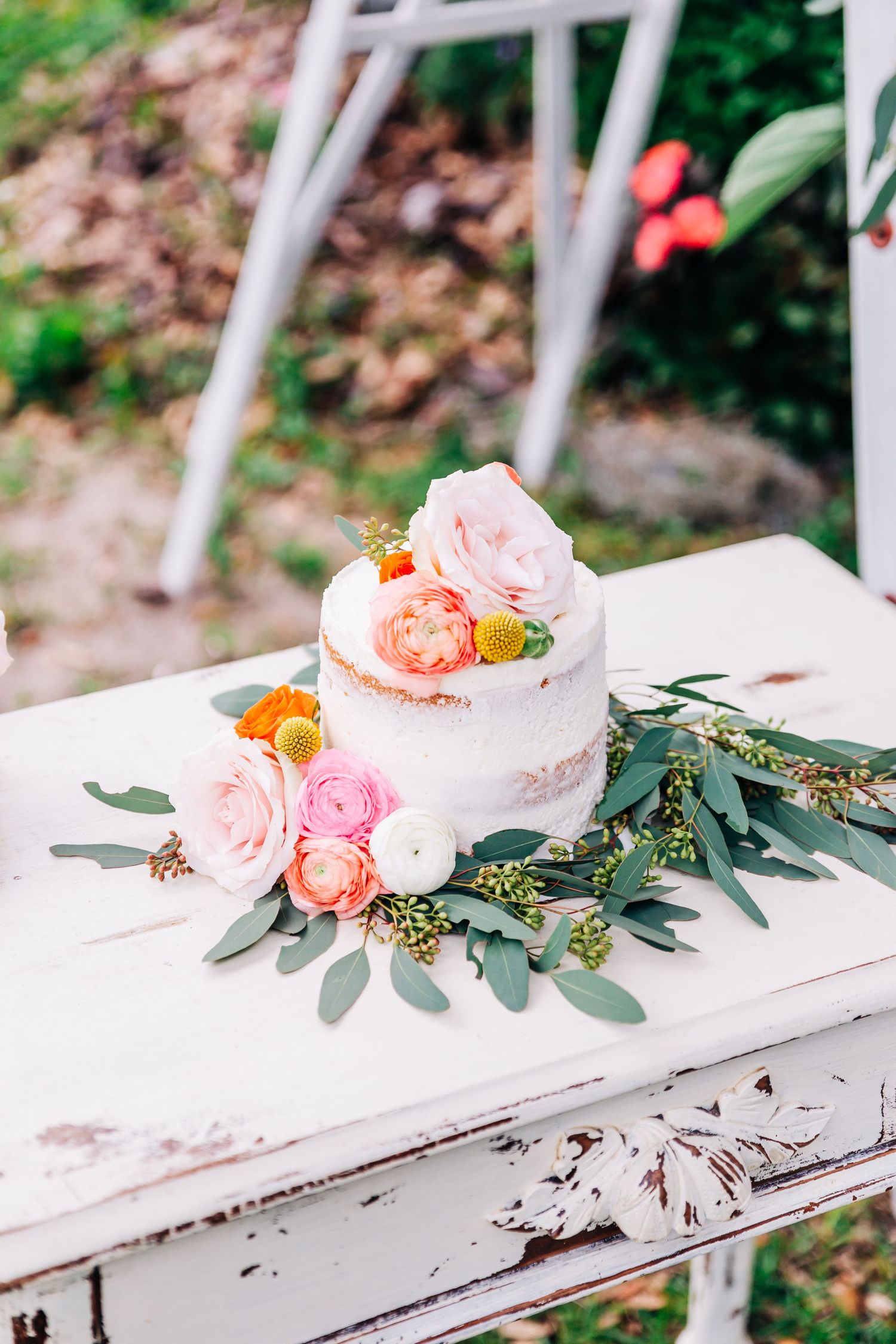 White wedding cake decorated with pink roses and greenery sits on a distressed vintage table.