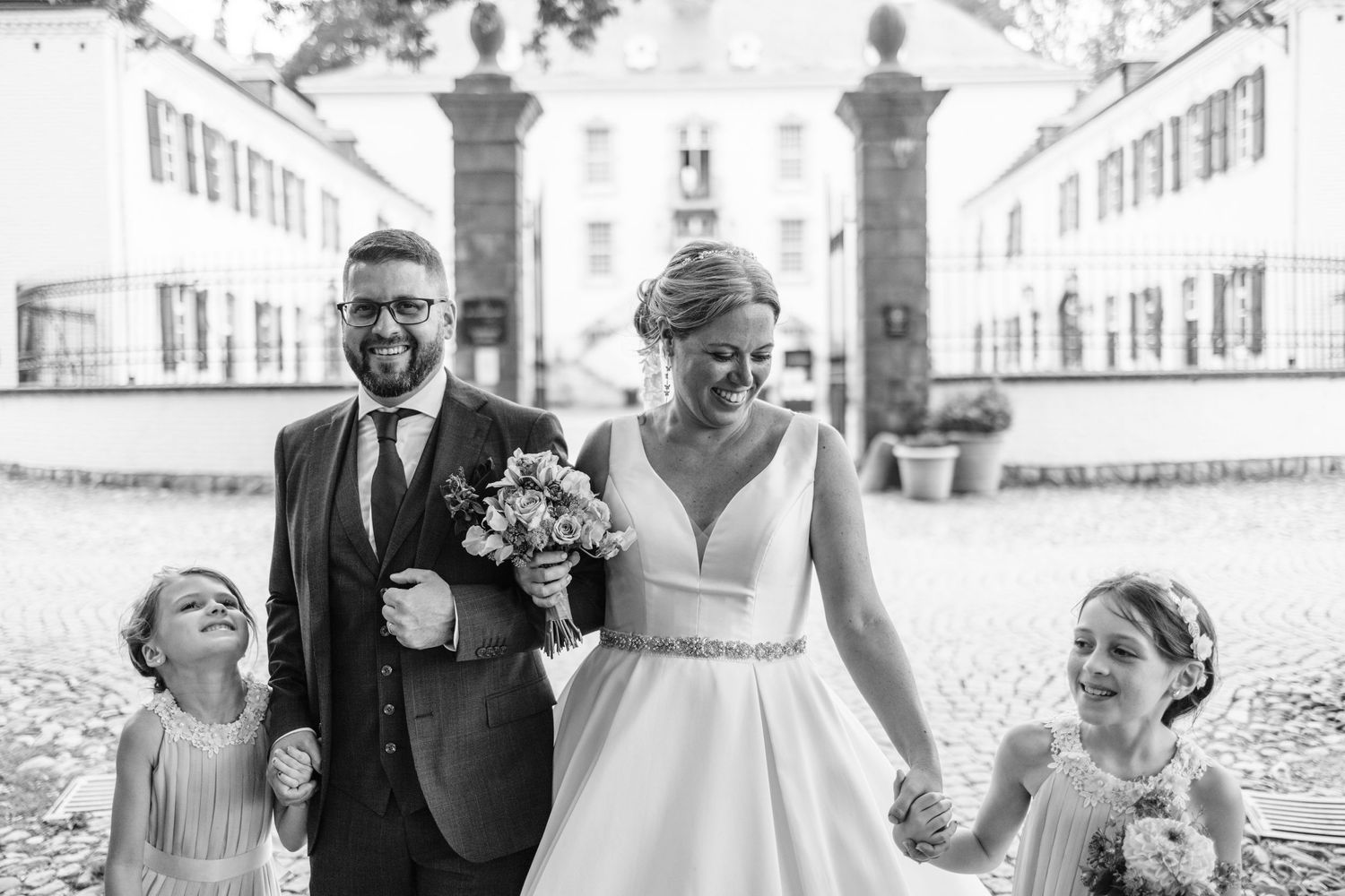 A wedding party walking together between stone pillars on a sunny day.