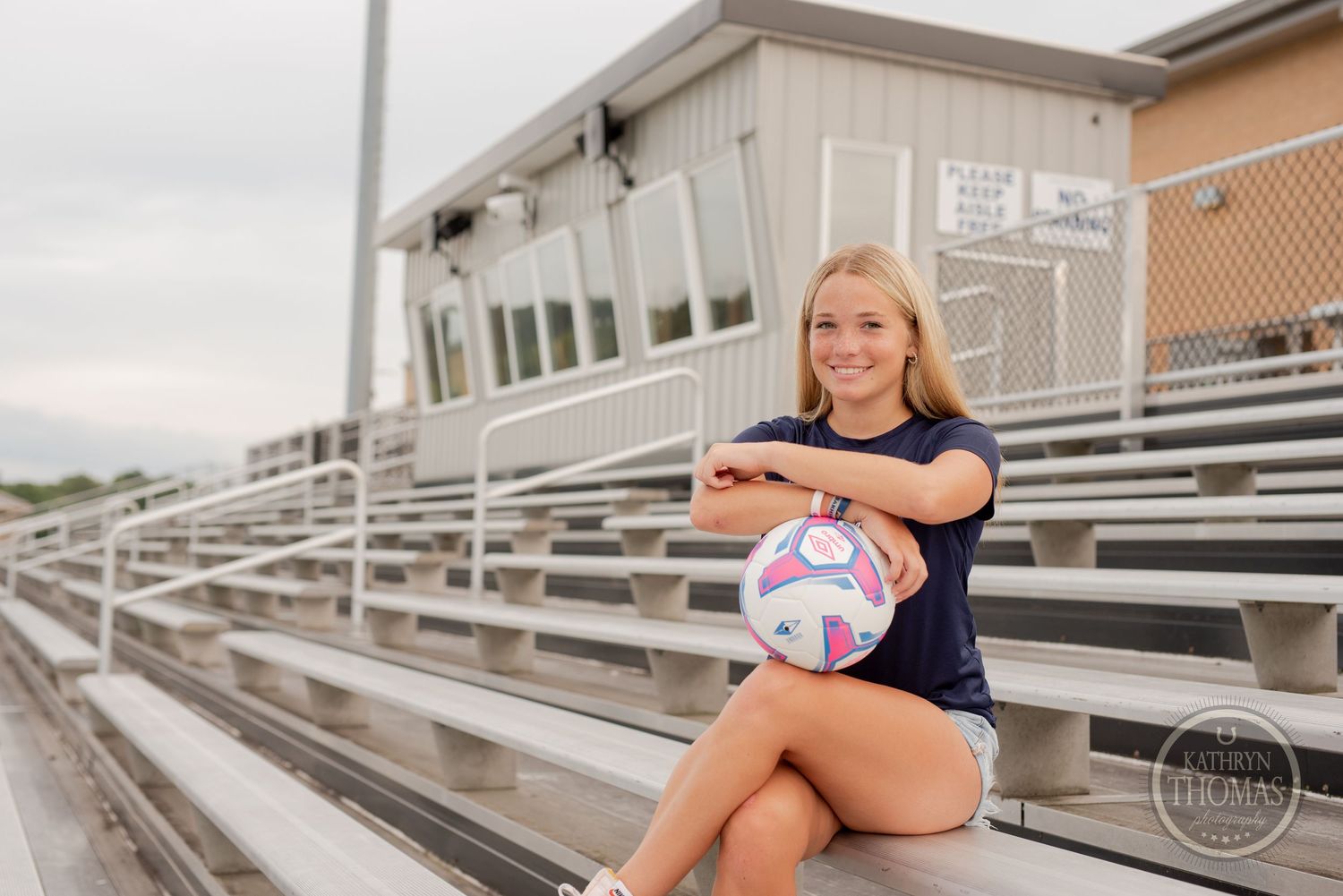 Soccer player with ball posing on metal bleachers during outdoor sports photoshoot.
