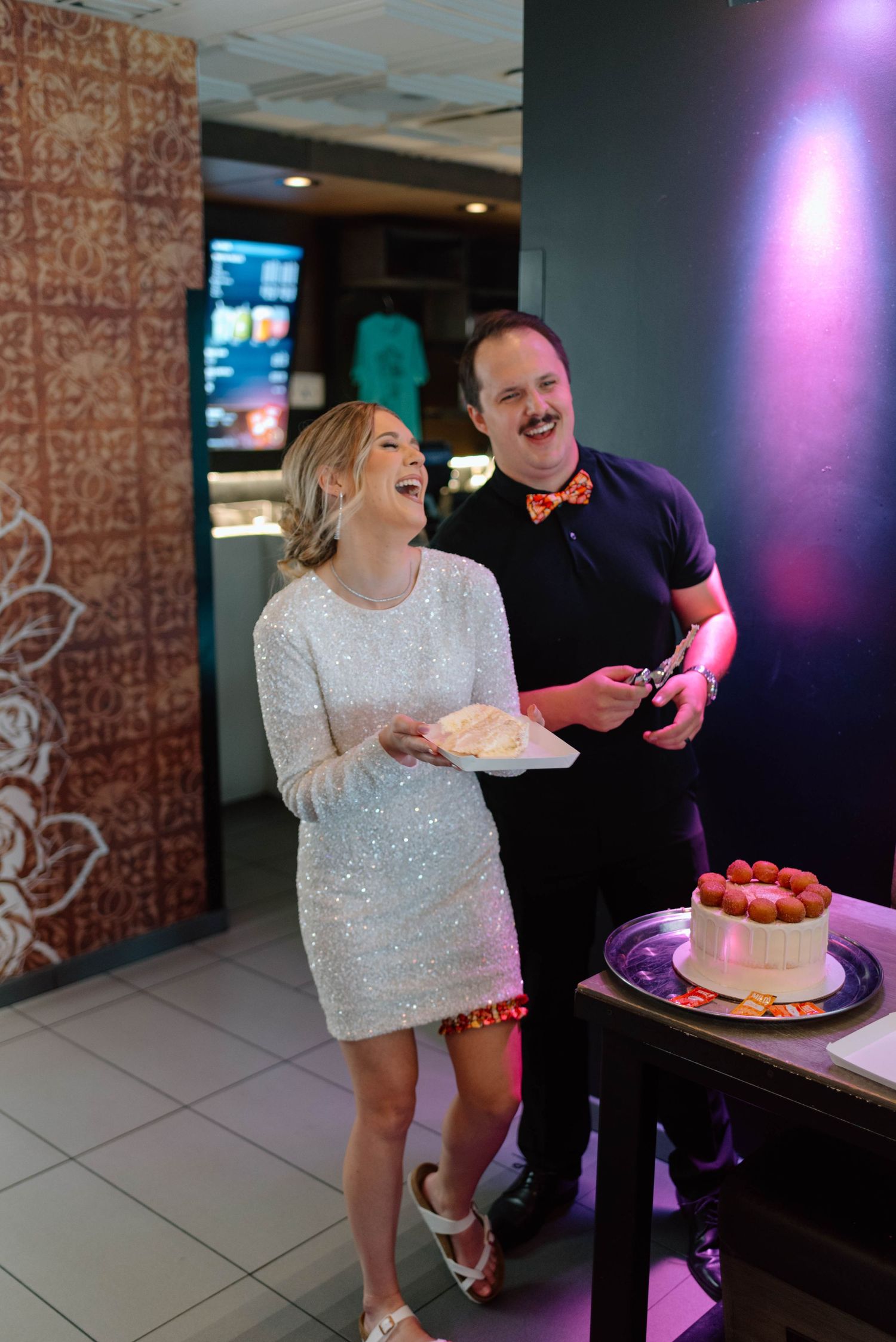A bride in a short sparkling dress  and groom in all black cut their Cinnabon cake during a Las Vegas elopement