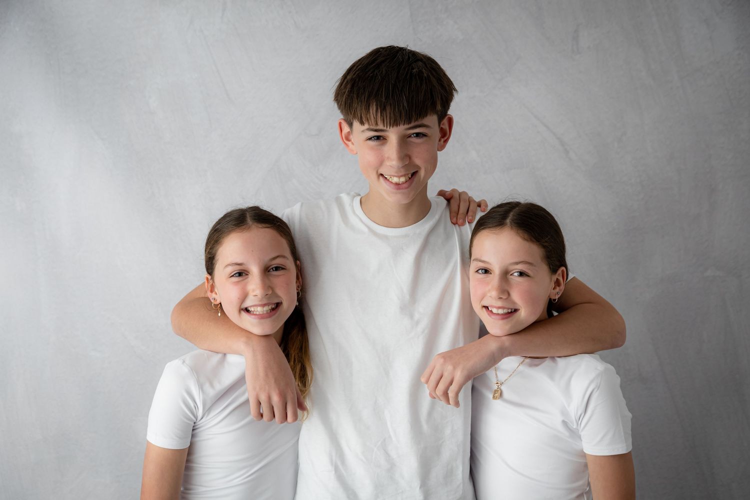 Studio portrait of three siblings in white shirts against grey background.