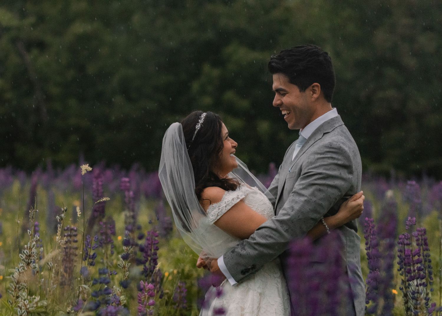 A couple shares a romantic moment in a field of vibrant purple lupine flowers during a summer wedding photoshoot in Colorado, U.S.A.