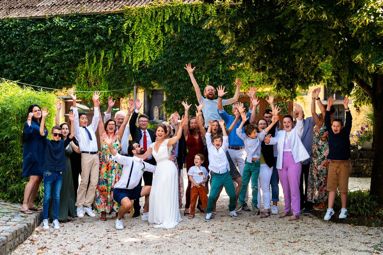 Large wedding group photo with guests jumping and celebrating outdoors.