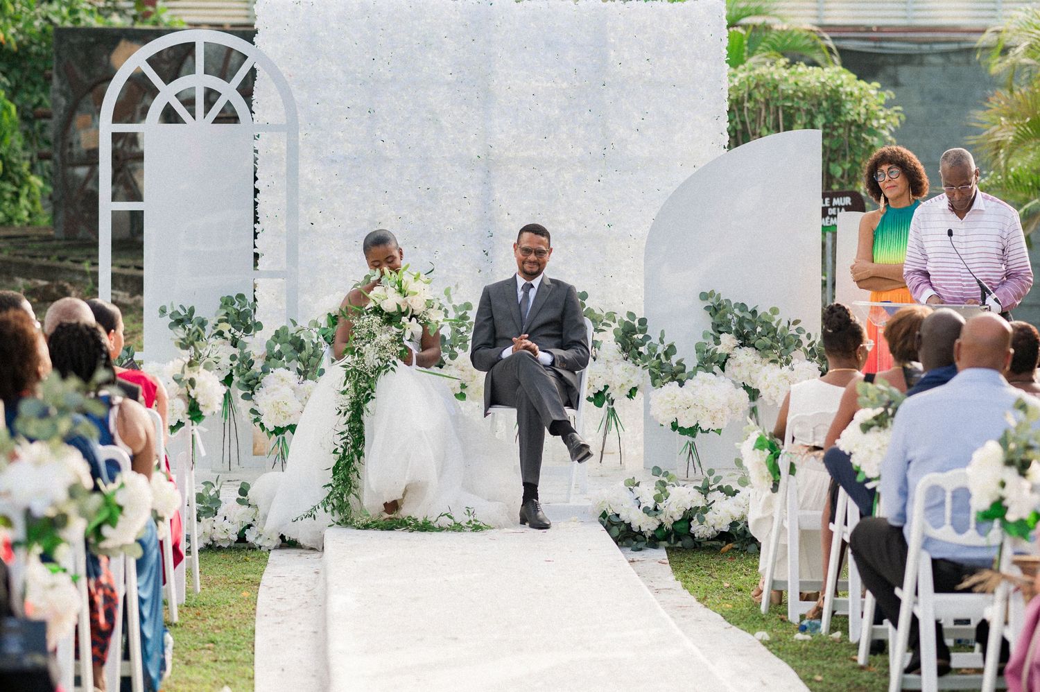 Couple de mariés en Guadeloupe, assis devant une décoration fleurie pendant la cérémonie laïque