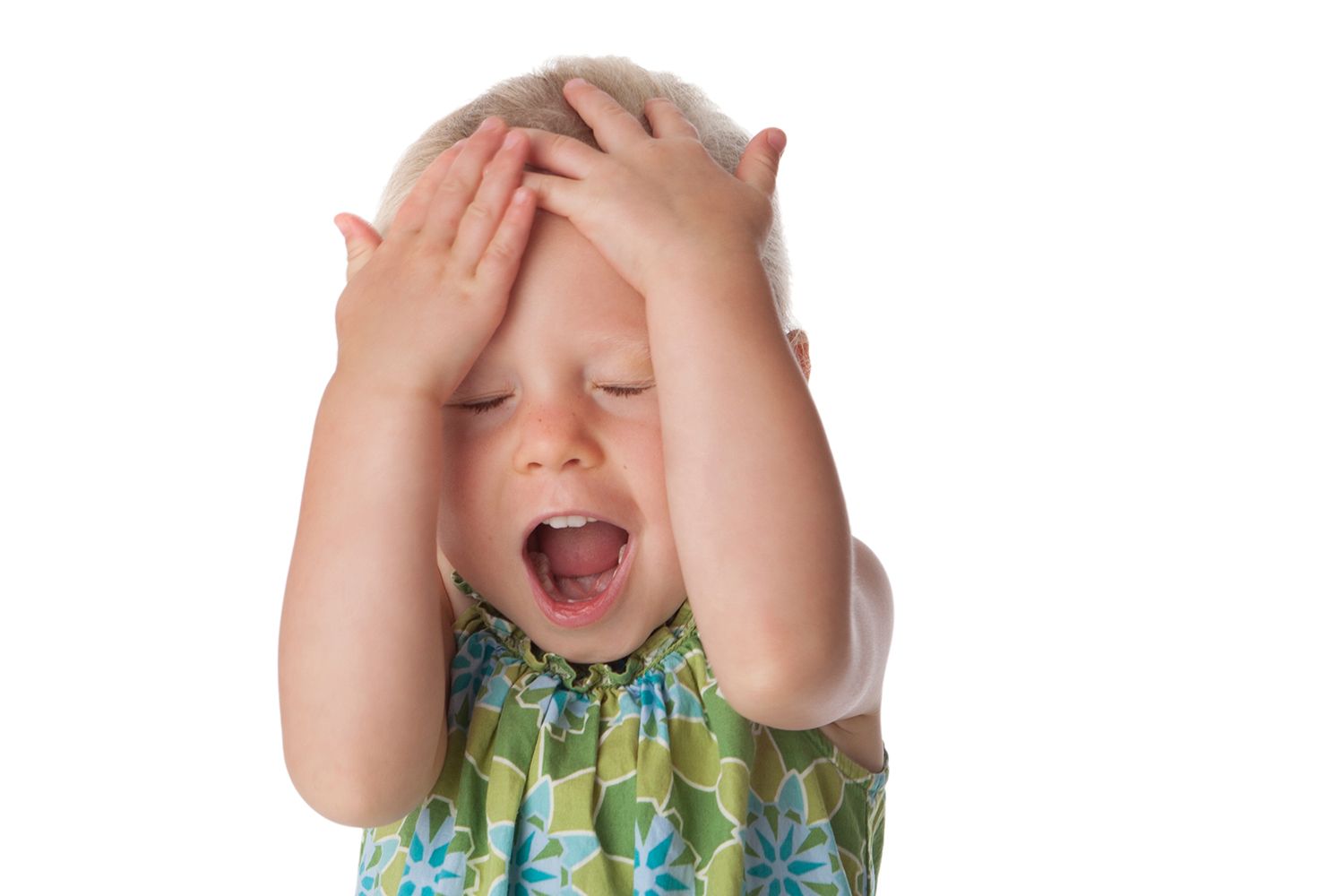 Young child covering face with hands while expressing playful emotion.